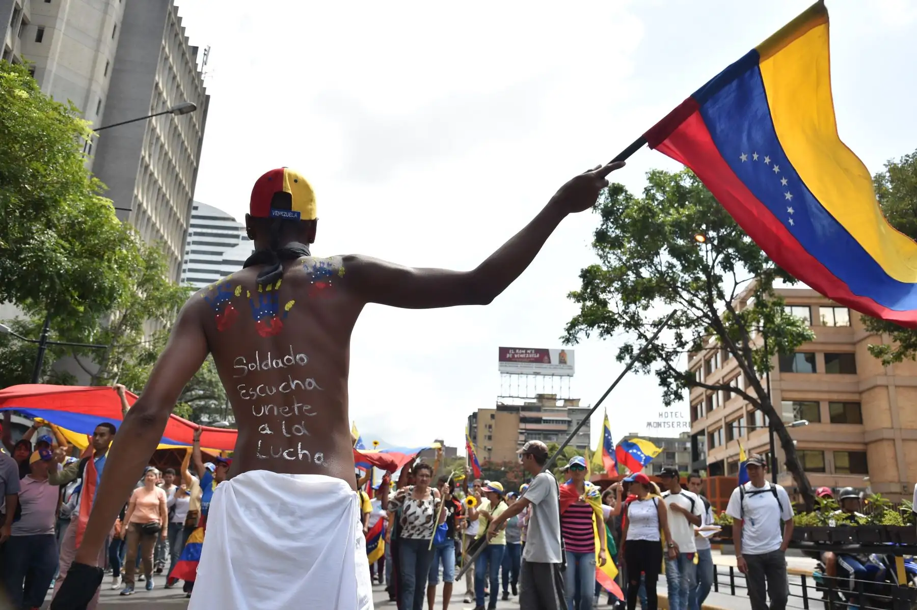 Un partidario del líder opositor venezolano y autoproclamado presidente interino Juan Guaido, con un mensaje en su espalda  "Soldado, escucha, únete a la lucha", ondea una bandera nacional venezolana durante una manifestación en Caracas . AFP