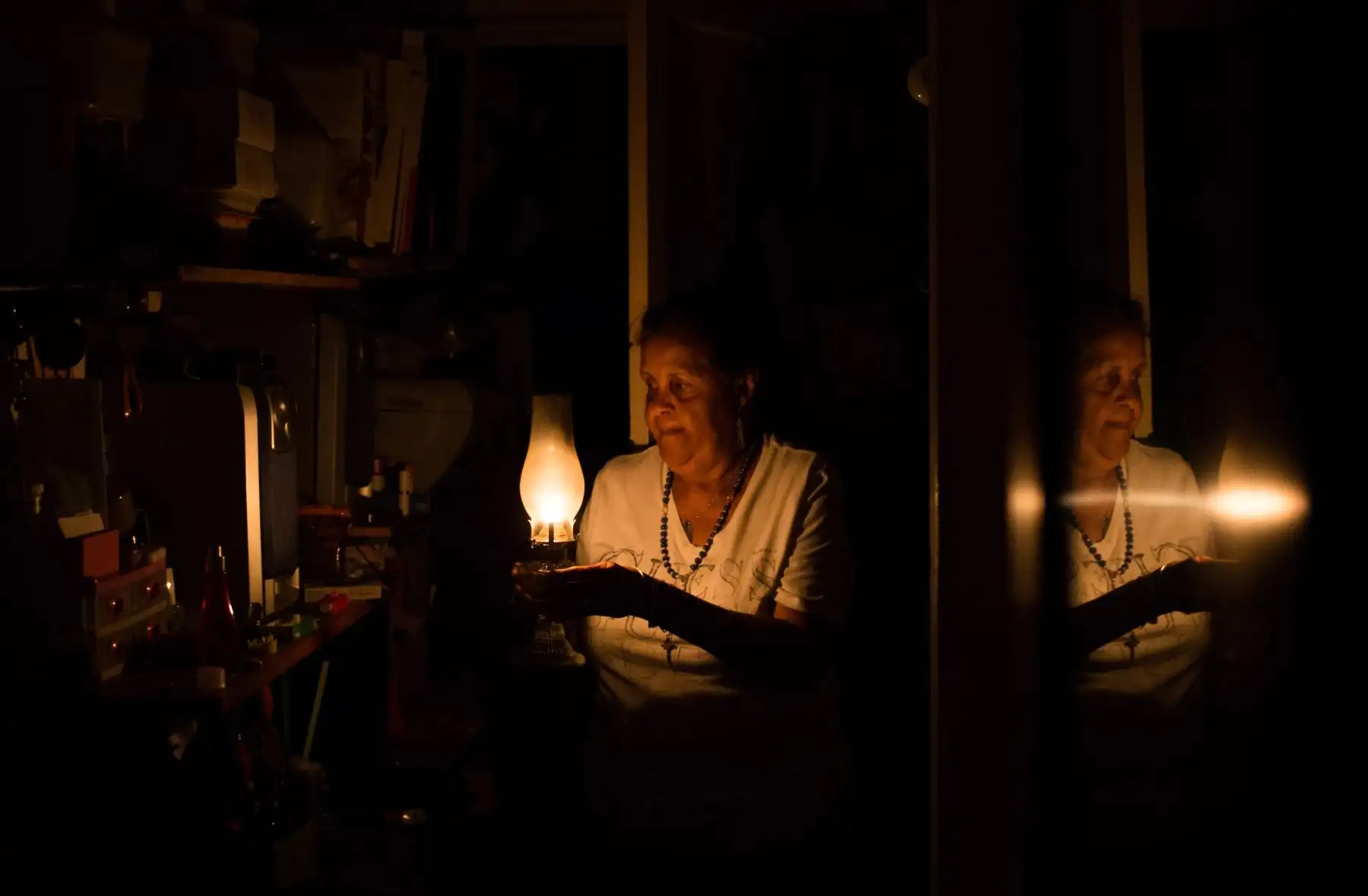 La venezolana Elvia Helena Lozano se refleja en un espejo mientras usa una lámpara de queroseno durante un apagón en su casa en Caracas. El domingo es el tercer día que los venezolanos permanecen sin comunicaciones, electricidad o agua, en un apagón sin precedentes que ya dejó 15 pacientes muertos y amenaza con extenderse indefinidamente, aumentando la angustia por la grave crisis política y económica que golpea a la nación sudamericana rica en petróleo. Foto: AFP