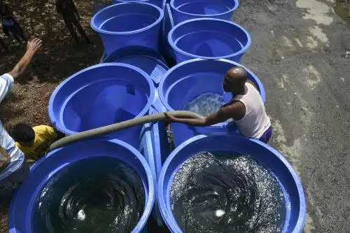 Los hombres trabajan llenando contenedores con agua potable para ser distribuidos en hospitales y vecindarios por el gobierno del presidente Nicolás Maduro, luego de un corte de energía masivo que agravó la escasez de agua en Caracas, el 13 de marzo de 2019. Foto: AFP
