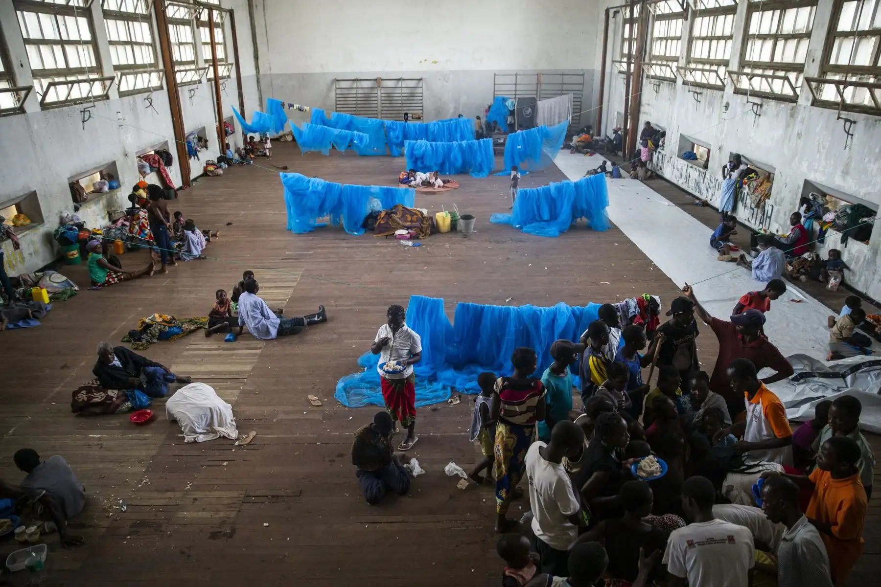 Lla gente se reúne para recibir la comida que reciben las personas desplazadas en una sala donde viven en la escuela secundaria Samora Machel en Beira, Mozambique. La escuela secundaria Samora Machelle es uno de los lugares que se utiliza como espacio vital para personas de Buzi, Mozambique que han sido desplazadas por las inundaciones causadas por el ciclón Idai.Foto: AFP
