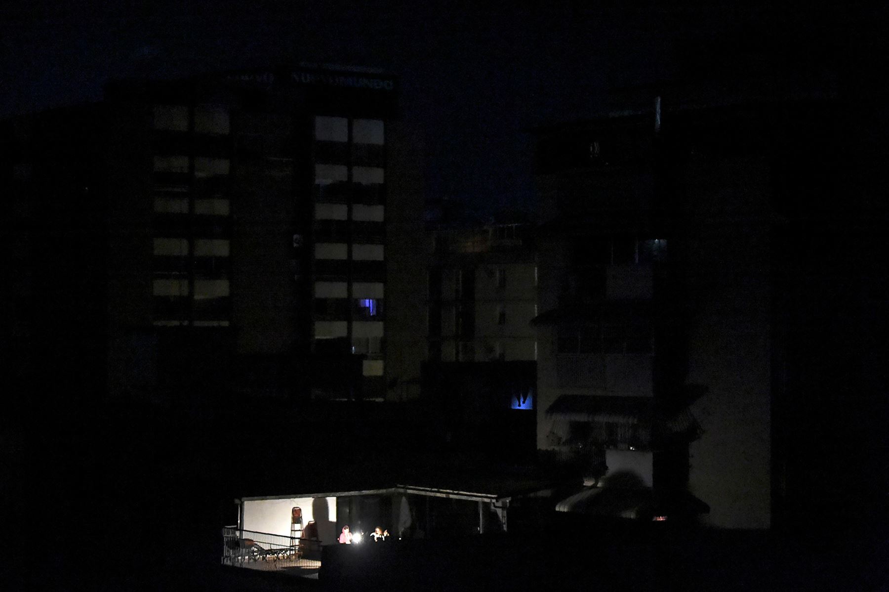 La gente se sienta alrededor de una lámpara de luz afuera de su casa durante un apagón en Caracas el 25 de marzo de 2019. Foto: AFP