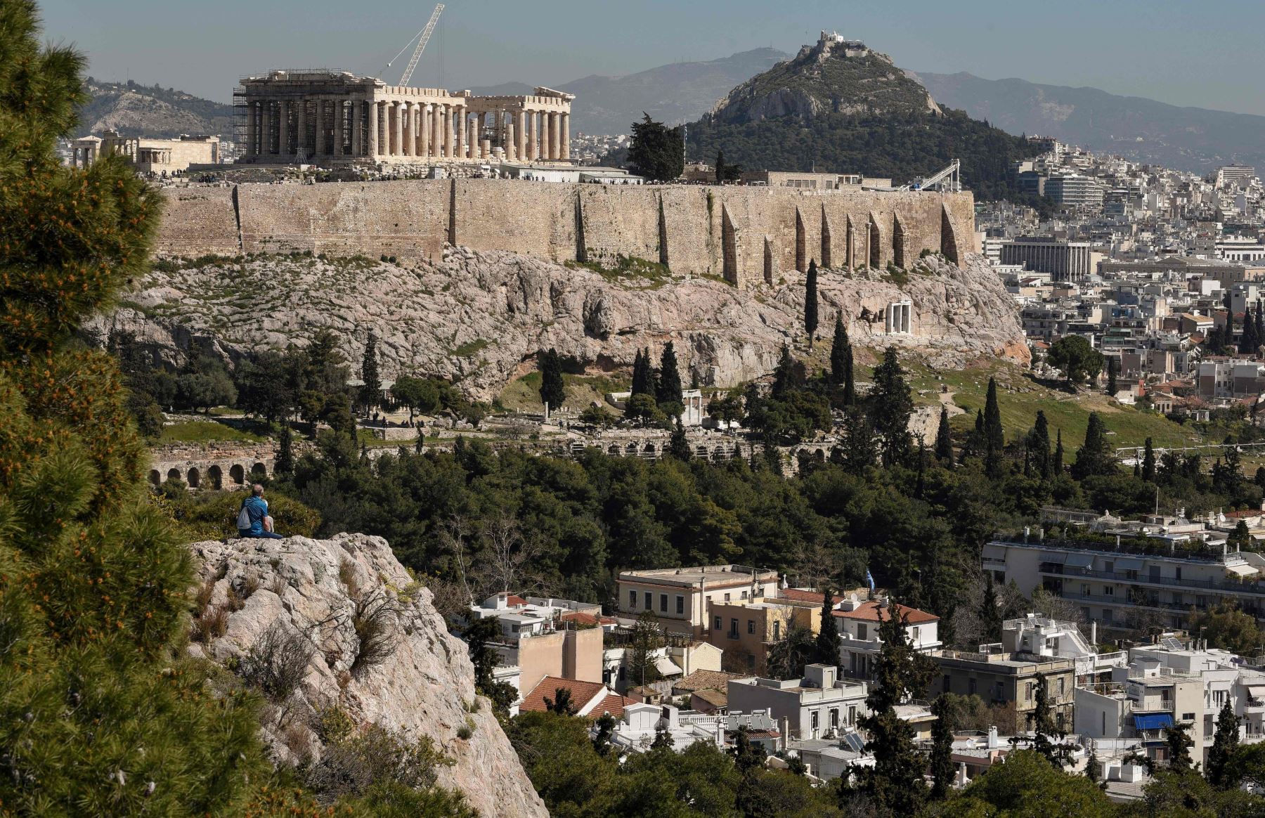 Un turista se sienta el 18 de marzo de 2019 en la colina de Filopappou en Atenas, debajo de la Acrópolis. Foto: AFP
