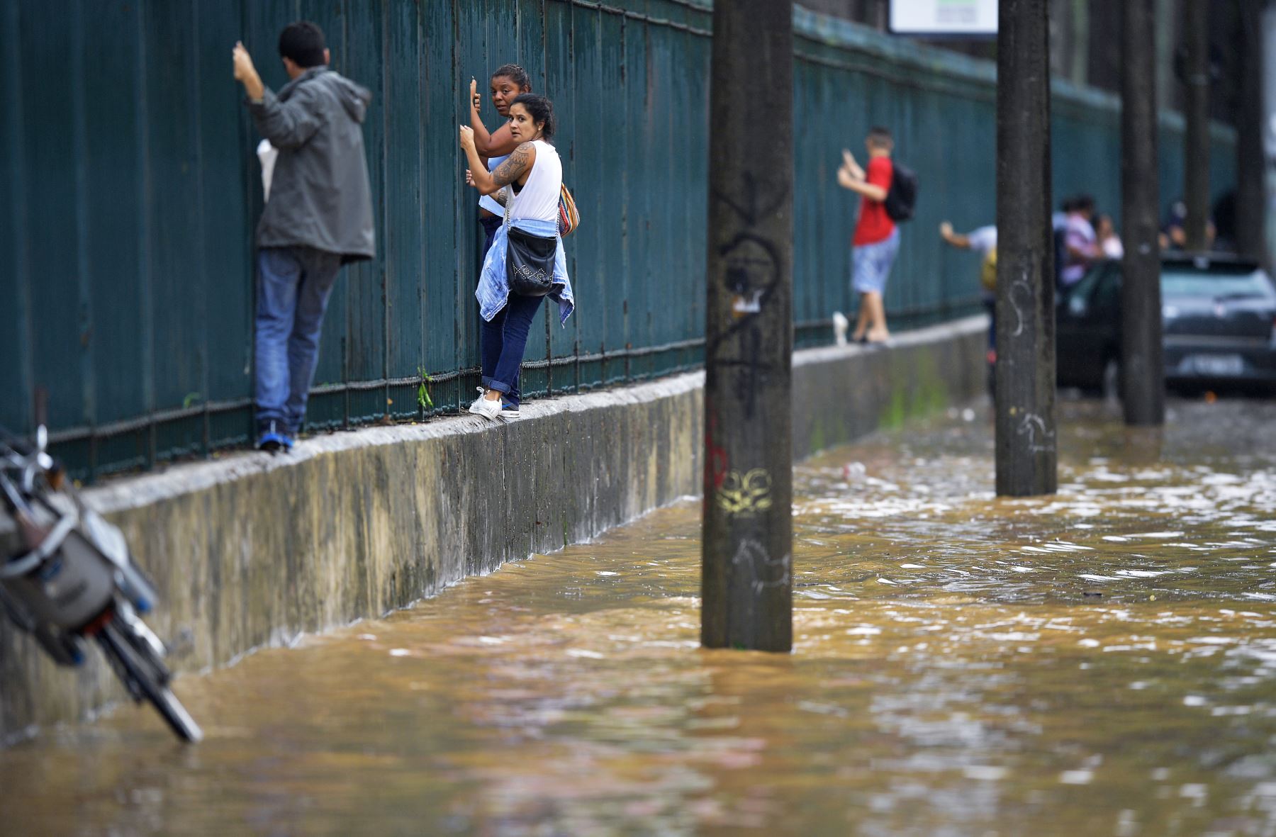 La gente sube a lo largo de una cerca para pasar por una área inundada en Río de Janeiro, Brasil. Foto: AFP