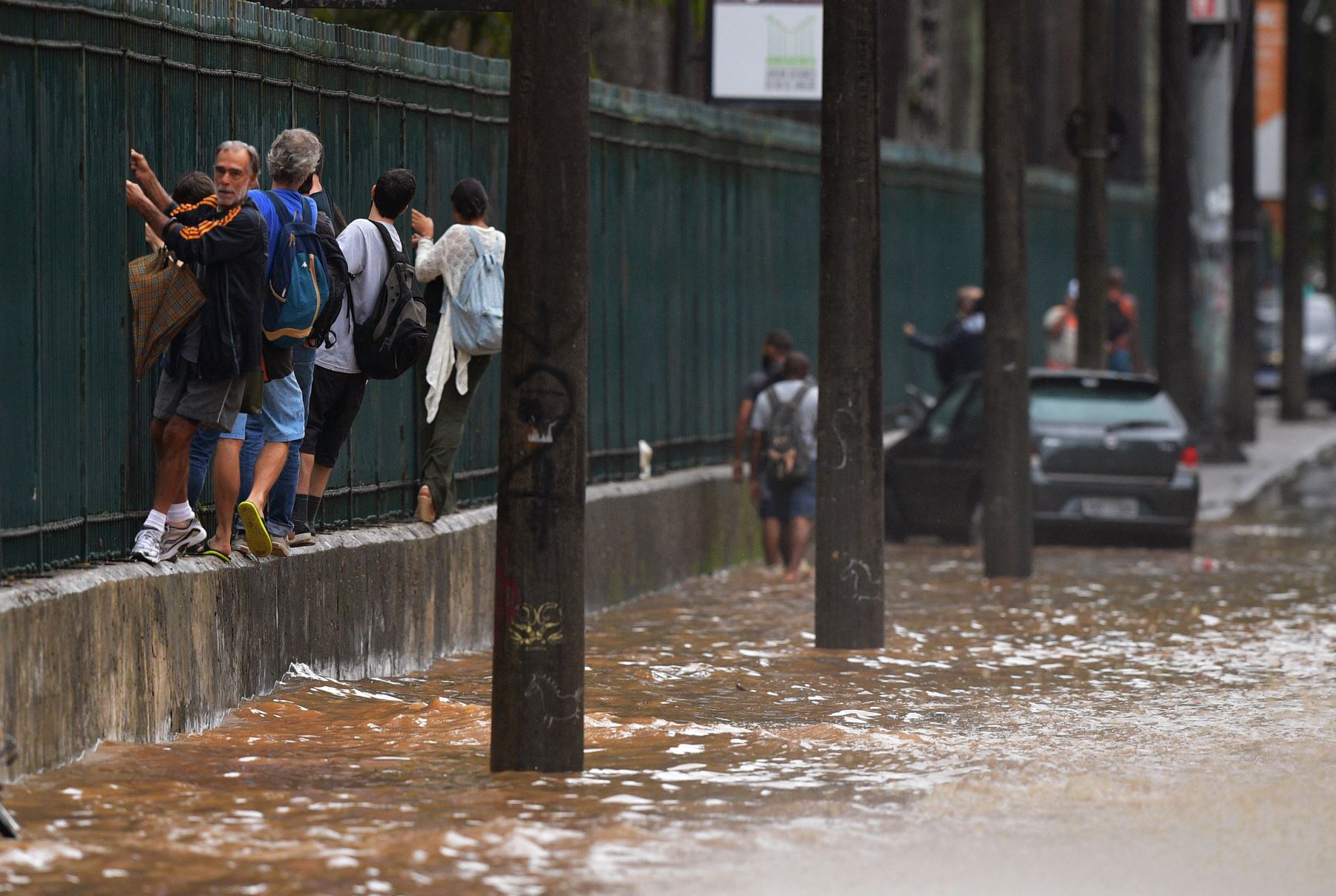 La gente sube a lo largo de una cerca para pasar por una área inundada en Río de Janeiro, Brasil. Foto: AFP