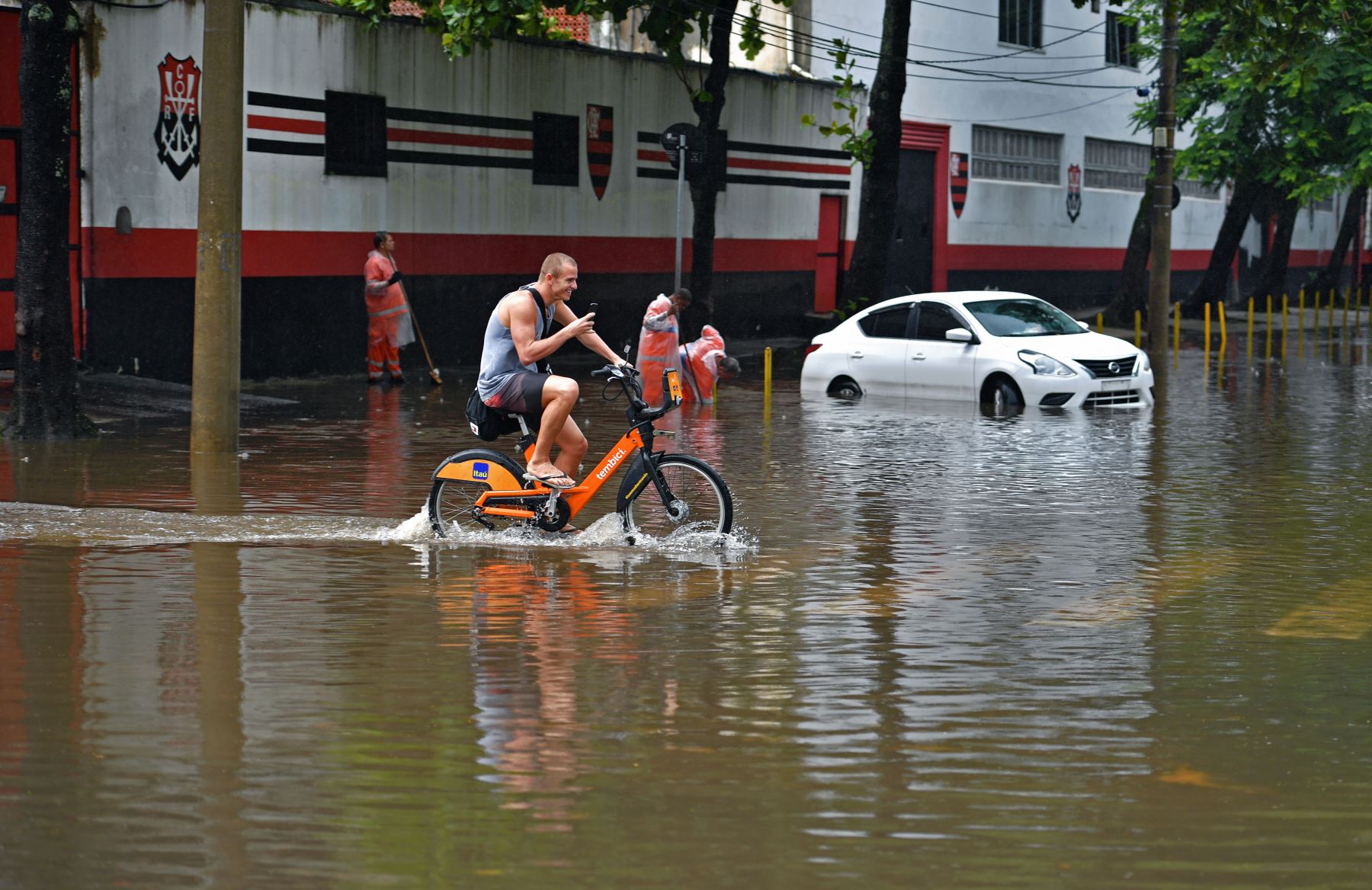 Trabajadores municipales intentan abrir un desagüe al lado de un automóvil varado en un área inundada en Río de Janeiro, Brasil. Foto: AFP