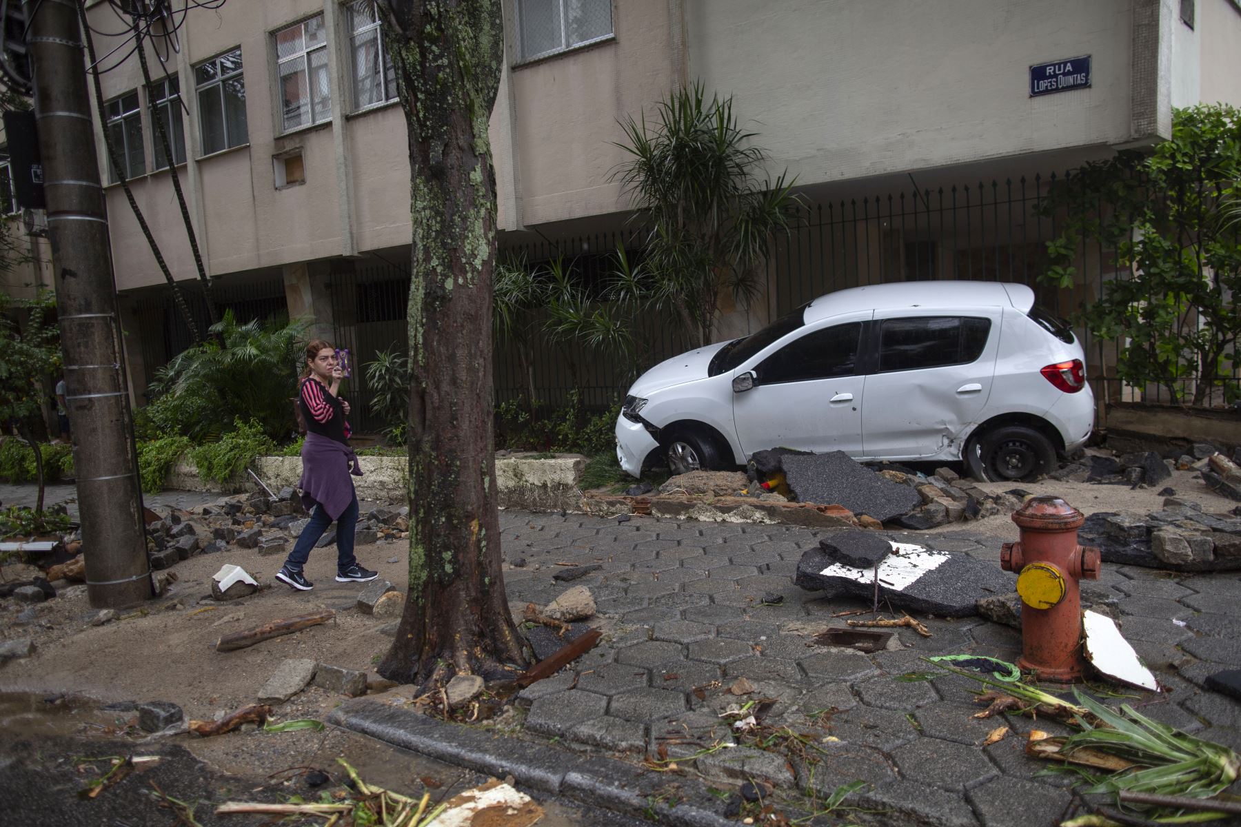 Una mujer toma una foto cerca de un automóvil dañado luego de fuertes lluvias en el vecindario Jardim Botanico en Río de Janeiro, Brasil. Foto: AFP