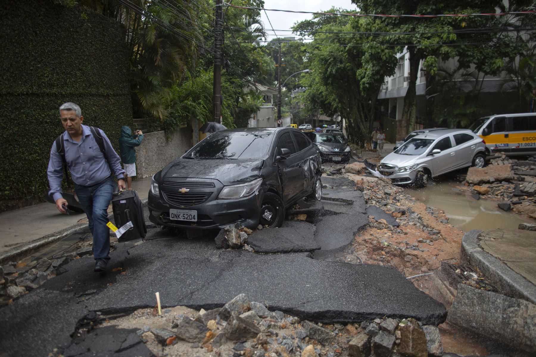 Un hombre camina cerca a los autos dañados luego de fuertes lluvias en el vecindario Jardim Botanico en Río de Janeiro, Brasil. Foto: AFP