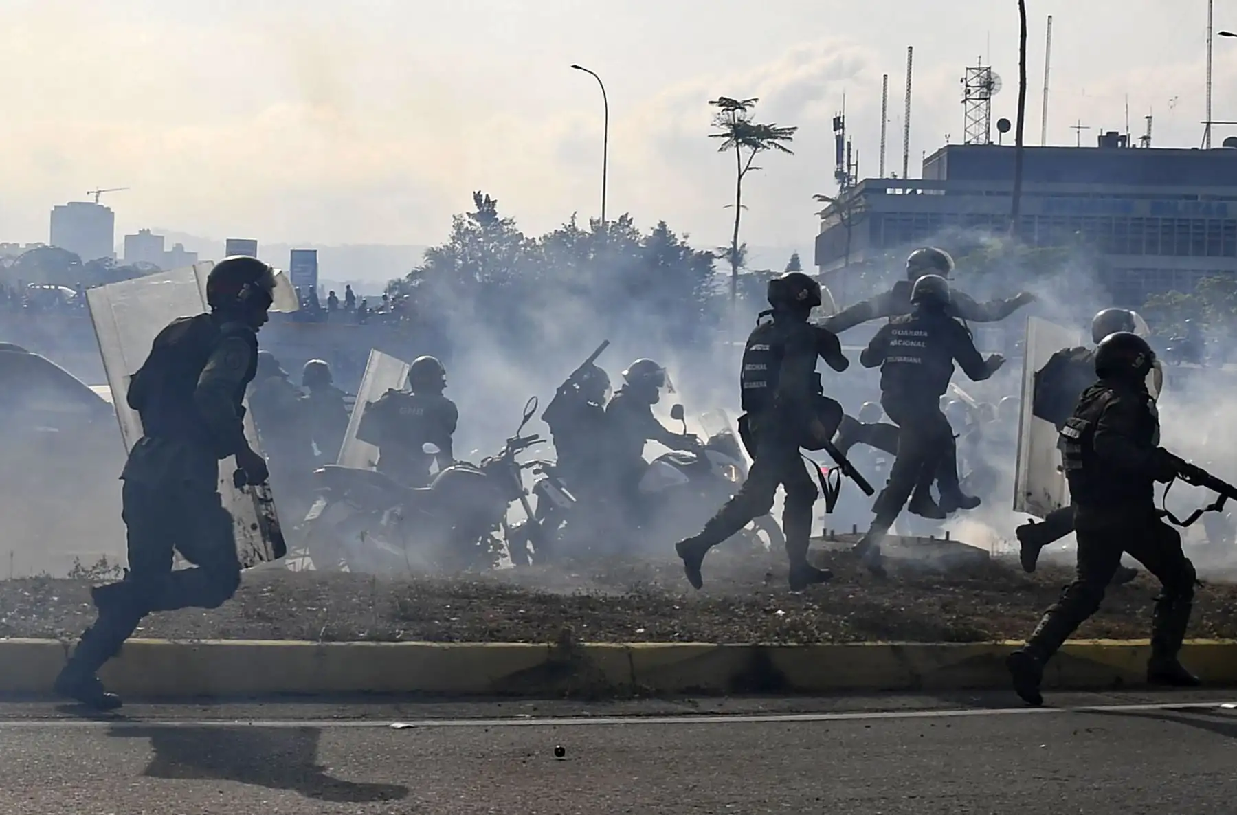 Miembros de la Guardia Nacional Bolivariana leales a Nicolás Maduro corren bajo una nube de gas lacrimógeno luego de ser rechazados por guardias que apoyan al presidente interino Juan Guaido, frente a la base militar de La Carlota en Caracas. Foto: AFP