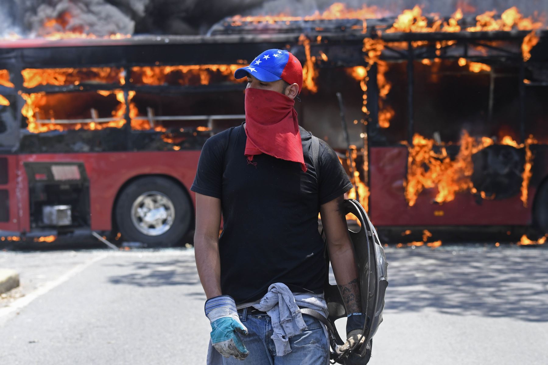 Manifestantes caminan cerca de un autobús en llamas durante los enfrentamientos con soldados leales a Nicolás Maduro. Foto: AFP