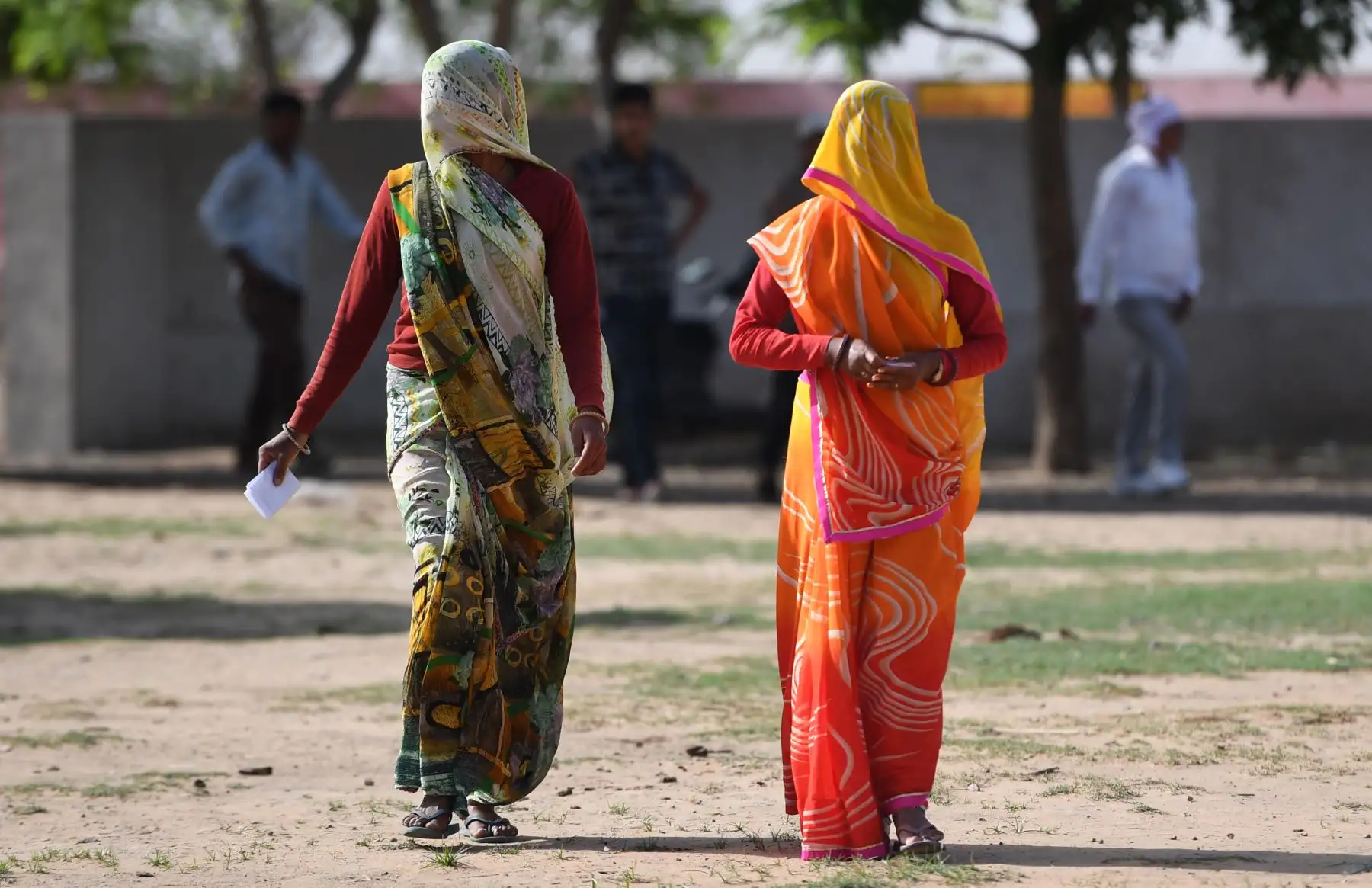 Mujeres de la India caminan frente a una fila de votantes edurante las elecciones generales de la India en el pueblo de Charanwala. Foto: AFP