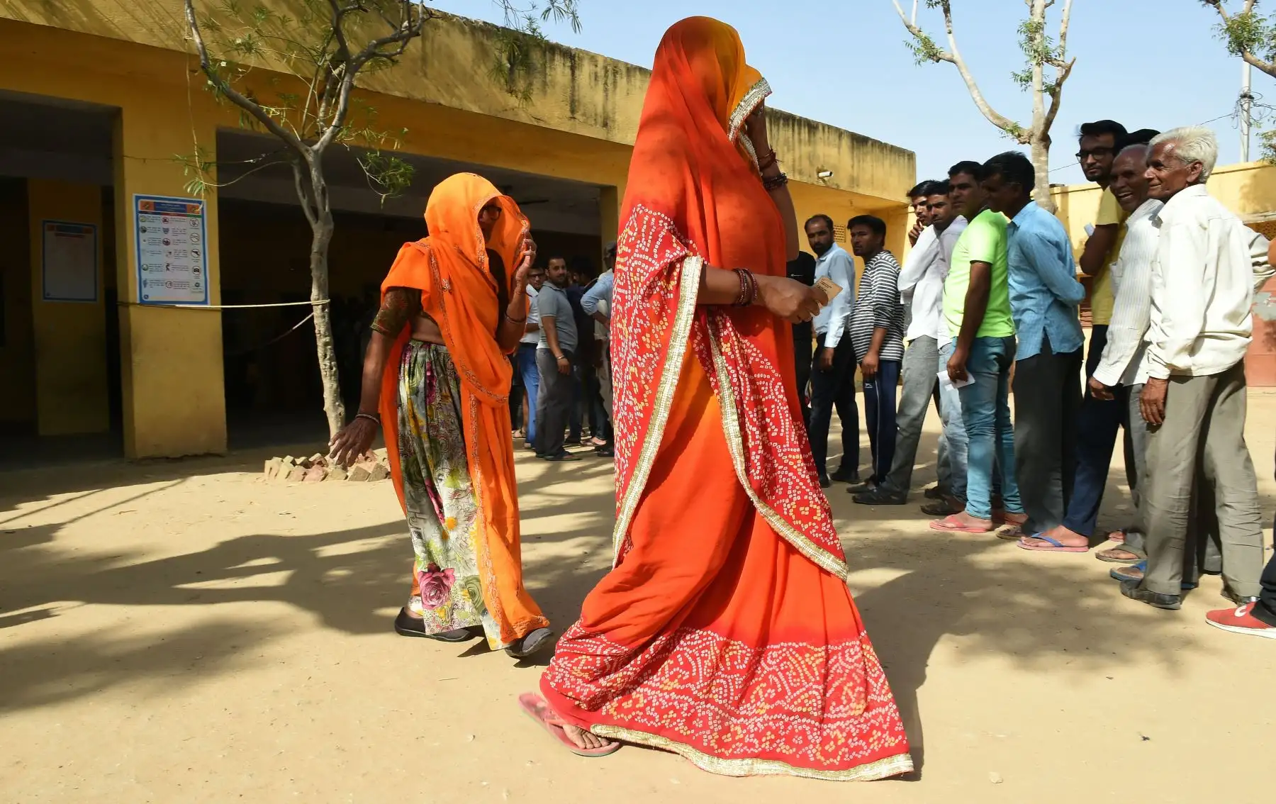 Mujeres de la India caminan frente a una fila de votantes edurante las elecciones generales de la India en el pueblo de Charanwala. Foto: AFP