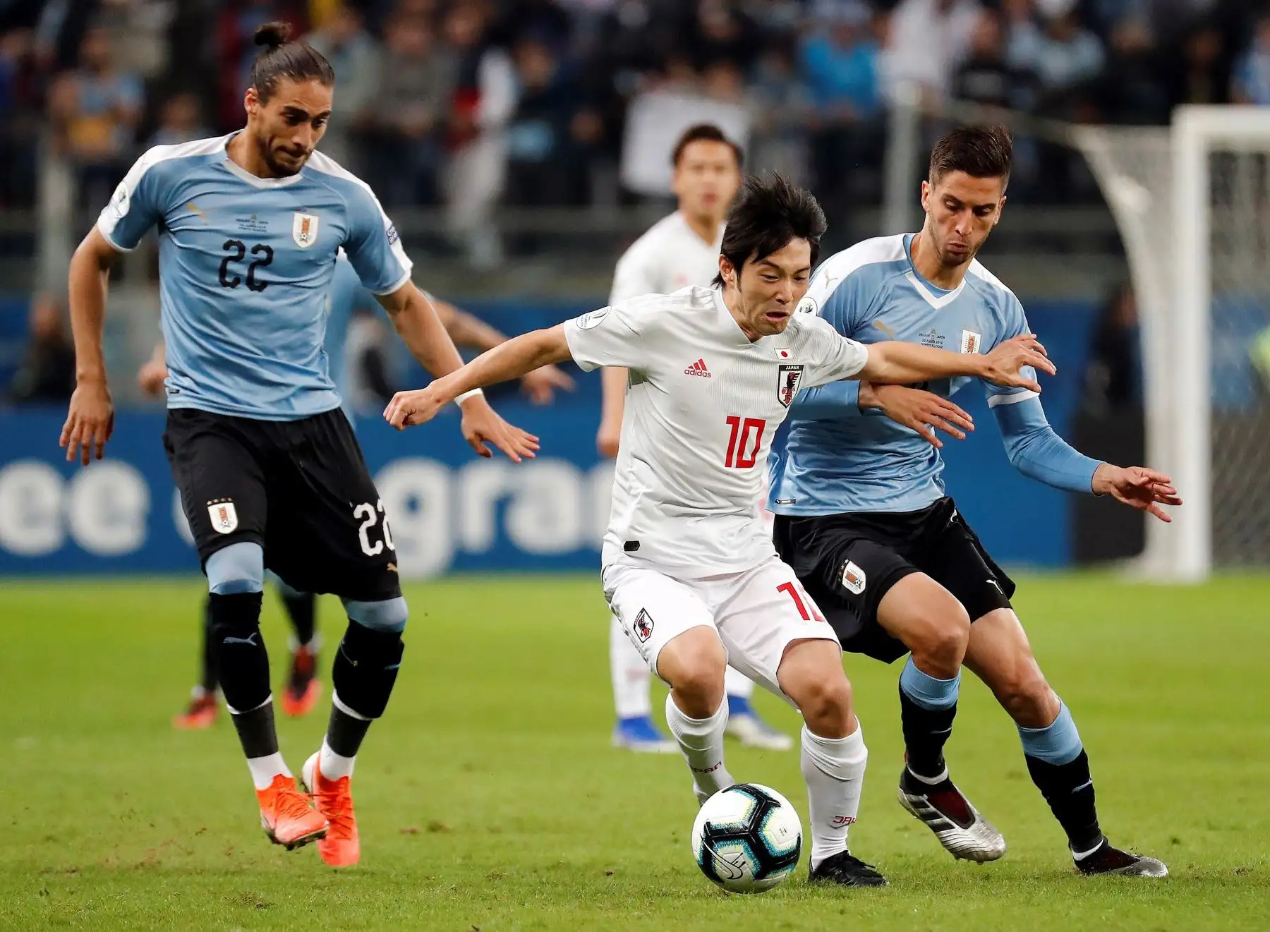 El jugador de Uruguay Martín Cáceres (i) disputa el balón con Shoya Nakajima (c) de Japón, durante el partido Uruguay-Japón del Grupo C de la Copa América de Fútbol 2019, en el Estadio Arena do Grêmio de Porto Alegre, Brasil.Foto.EFE