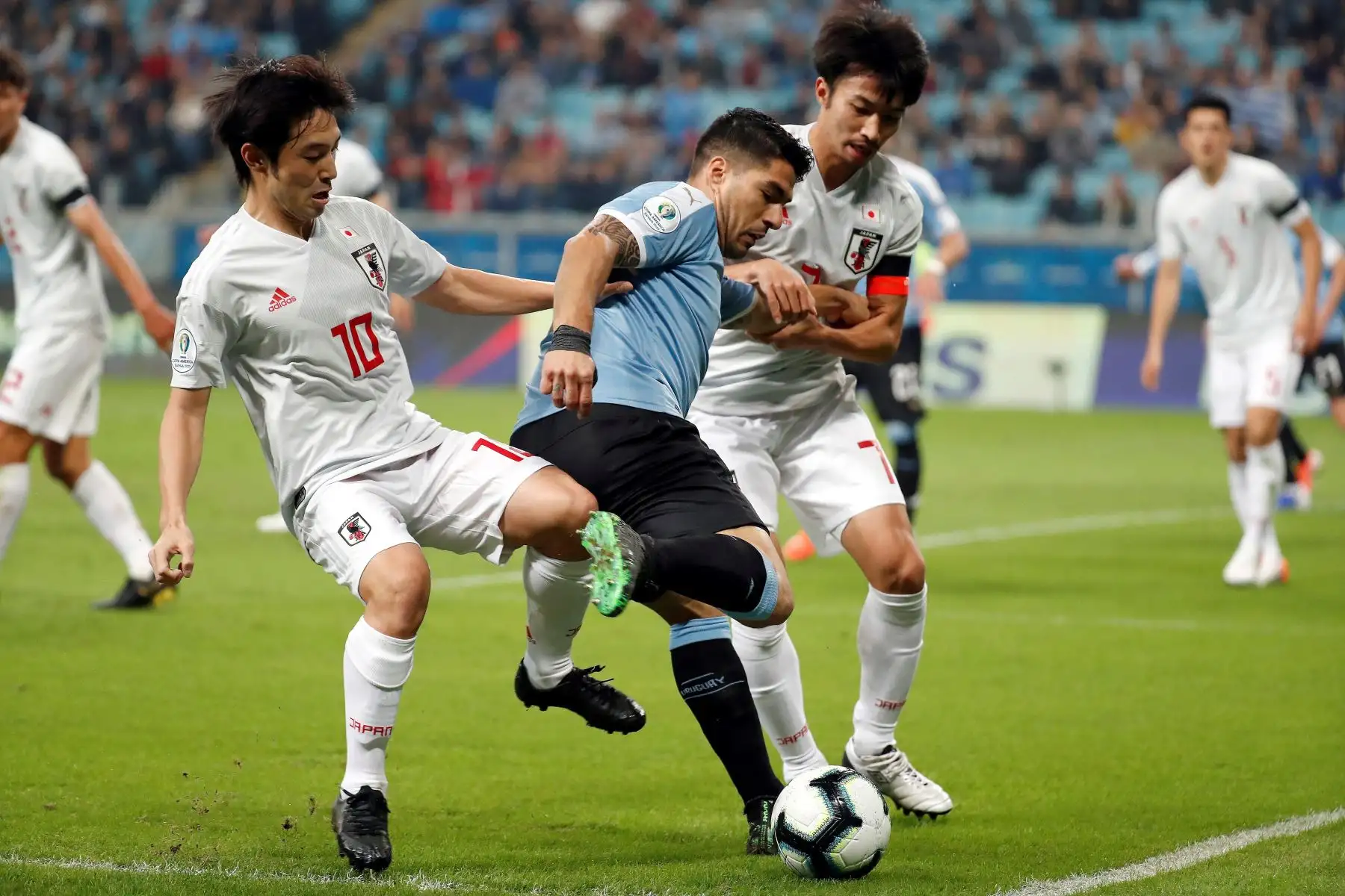 El jugador de Uruguay Luis Suárez (c) disputa el balón con Shoya Nakajima (i) yGaku Shibasaki (d) de Japón, durante el partido Uruguay-Japón del Grupo C de la Copa América de Fútbol 2019, en el Estadio Arena do Grêmio de Porto Alegre, Brasil.Foto:EFE