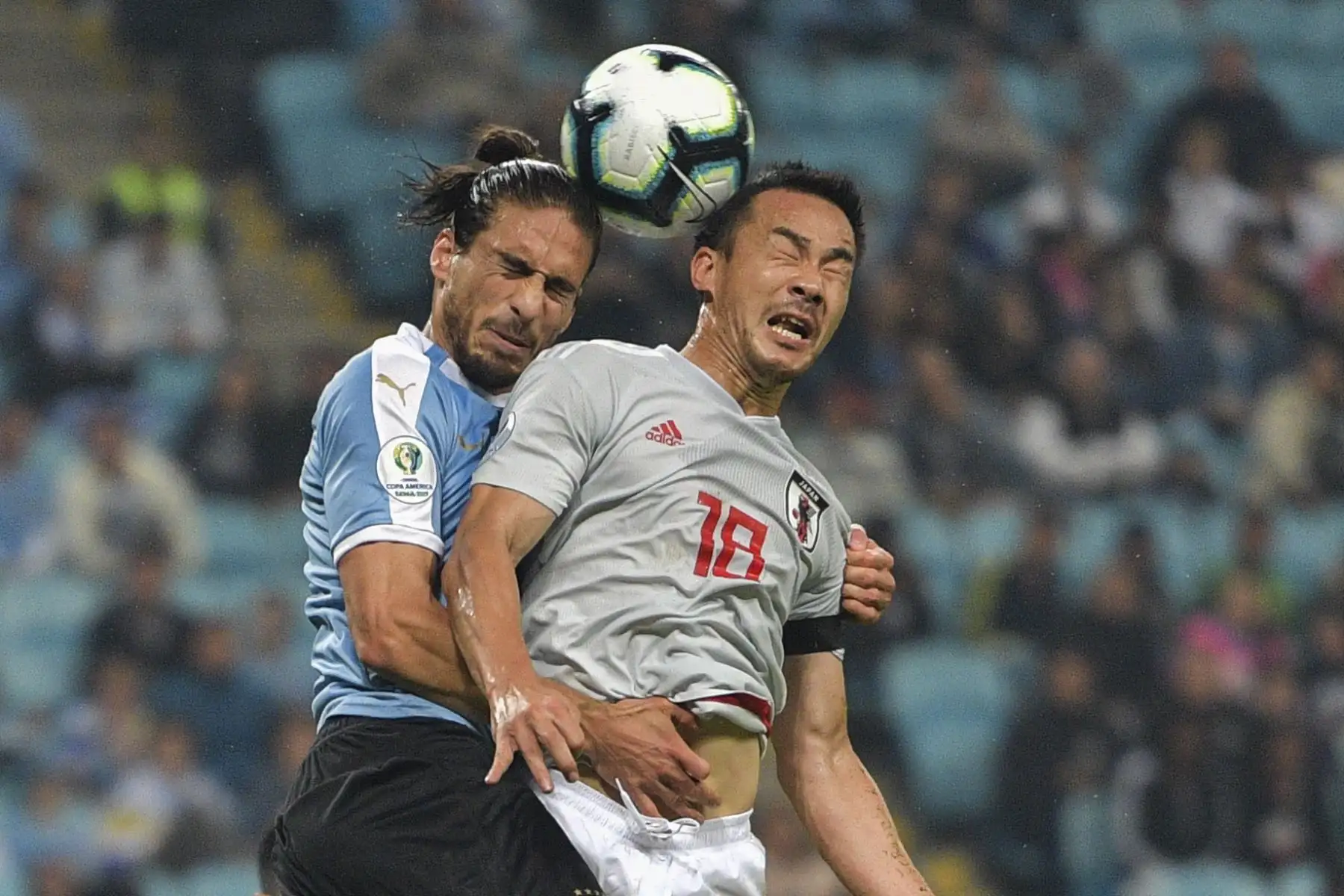 Martin Caceres de Uruguay, y Shinji Okazaki, de Japón, se lanzan a la cabeza durante el partido del Grupo C del torneo de fútbol de América en el estadio Gremio Arena en Porto Alegre, Brasil.Foto.AFP