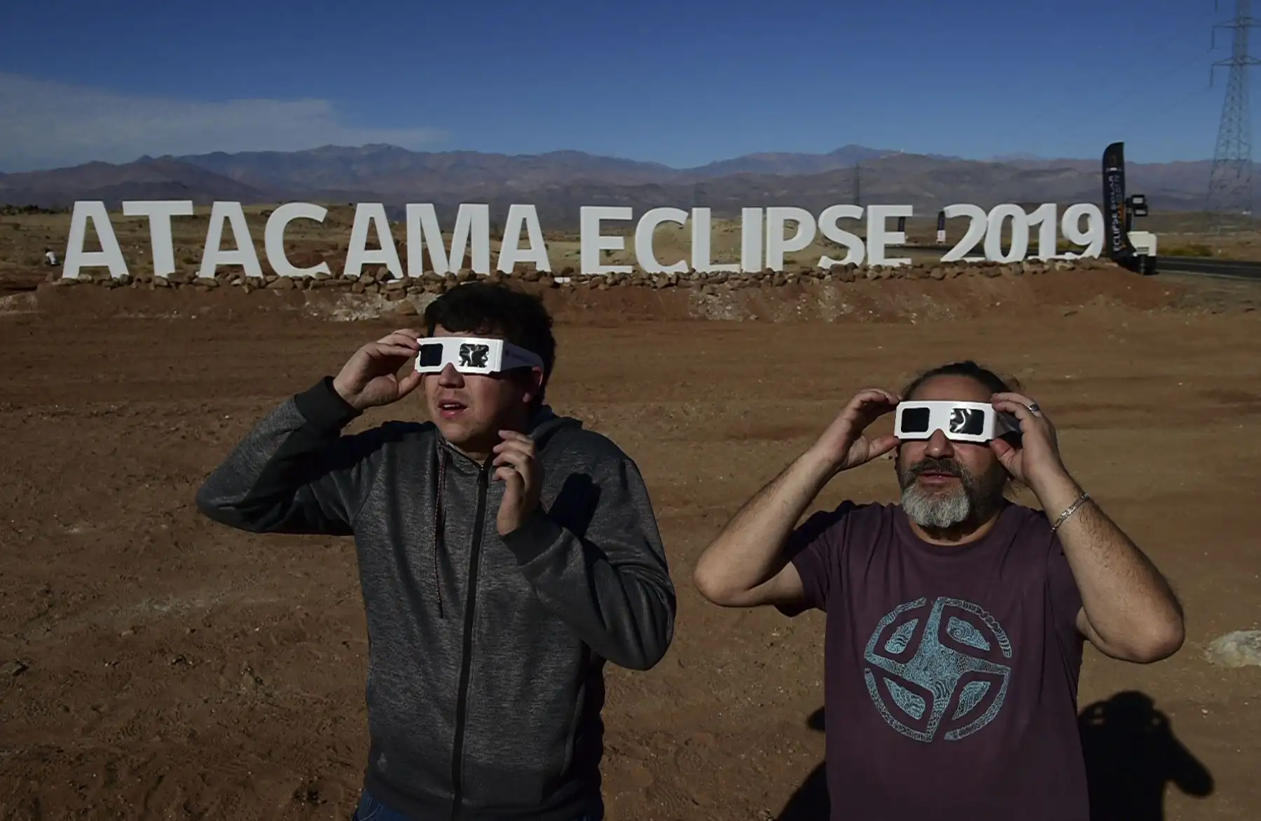Los turistas prueban gafas especiales para ver un eclipse en la entrada de un campamento astronómico que espera recibir a miles de turistas para observar el eclipse total de sol del 2 de julio, en la comuna de Vallenar, en el desierto de Atacama, a unos 600 km al norte de Santiago.
Foto: AFP