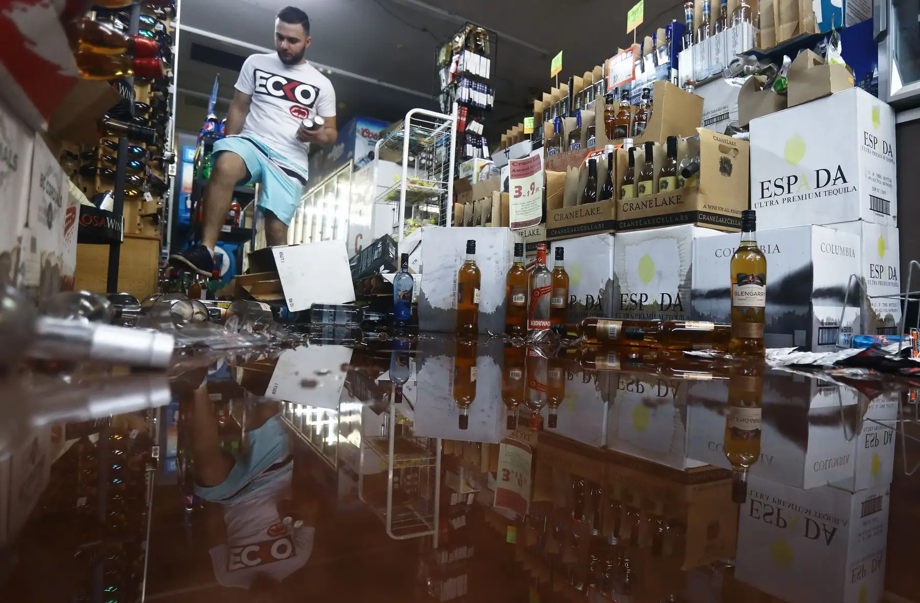 Un empleado lleva artículos para un cliente por botellas rotas dispersas en el piso, luego de un terremoto de magnitud 7.1 que golpeó  en Ridgecrest, California. 
Foto: AFP