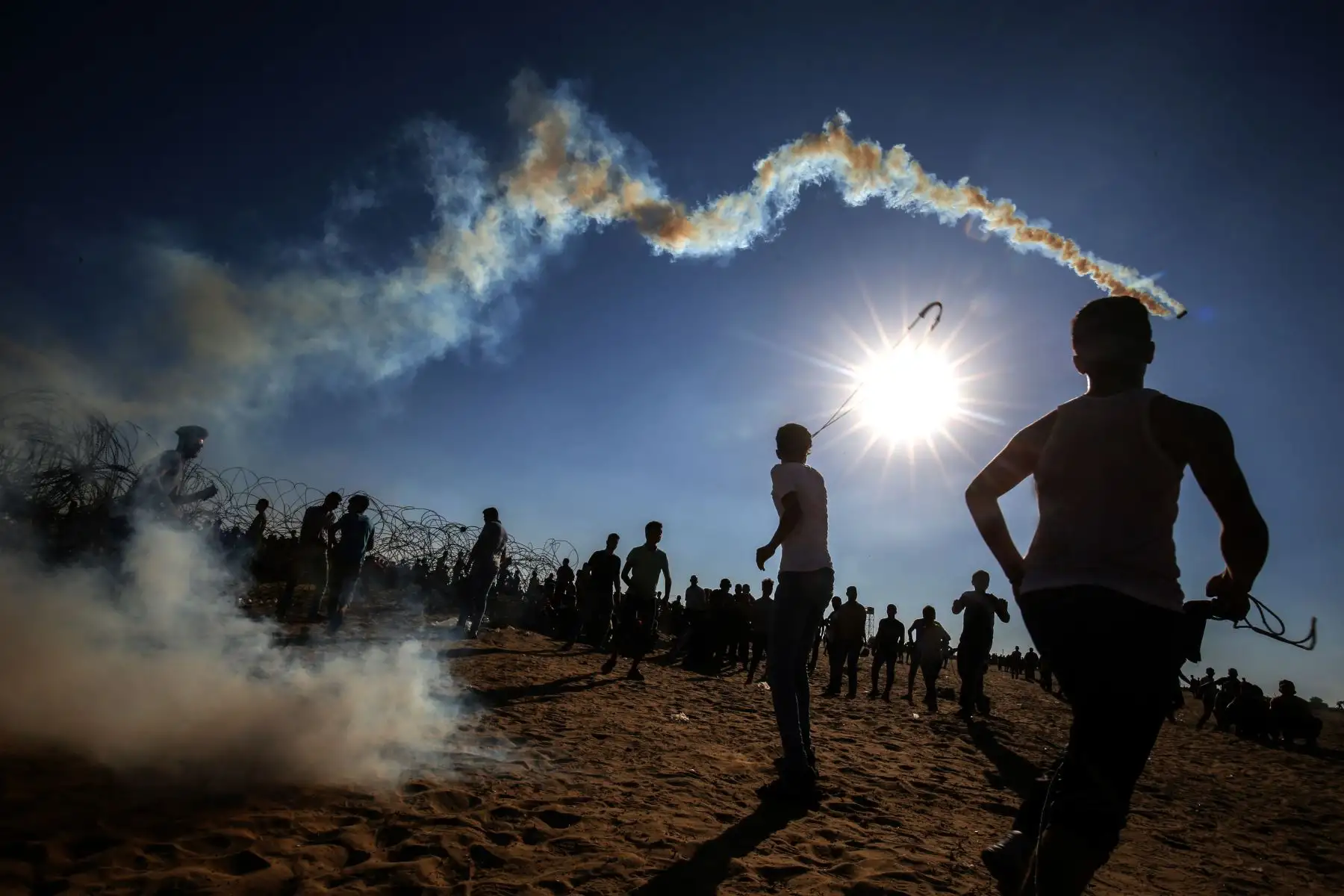 Los jóvenes palestinos usan hondas para lanzar rocas a las tropas israelíes durante los enfrentamientos entre manifestantes palestinos y fuerzas israelíes a través de la cerca de alambre de púas después de una manifestación fronteriza cerca de Rafah en el sur de la Franja de Gaza. AFP