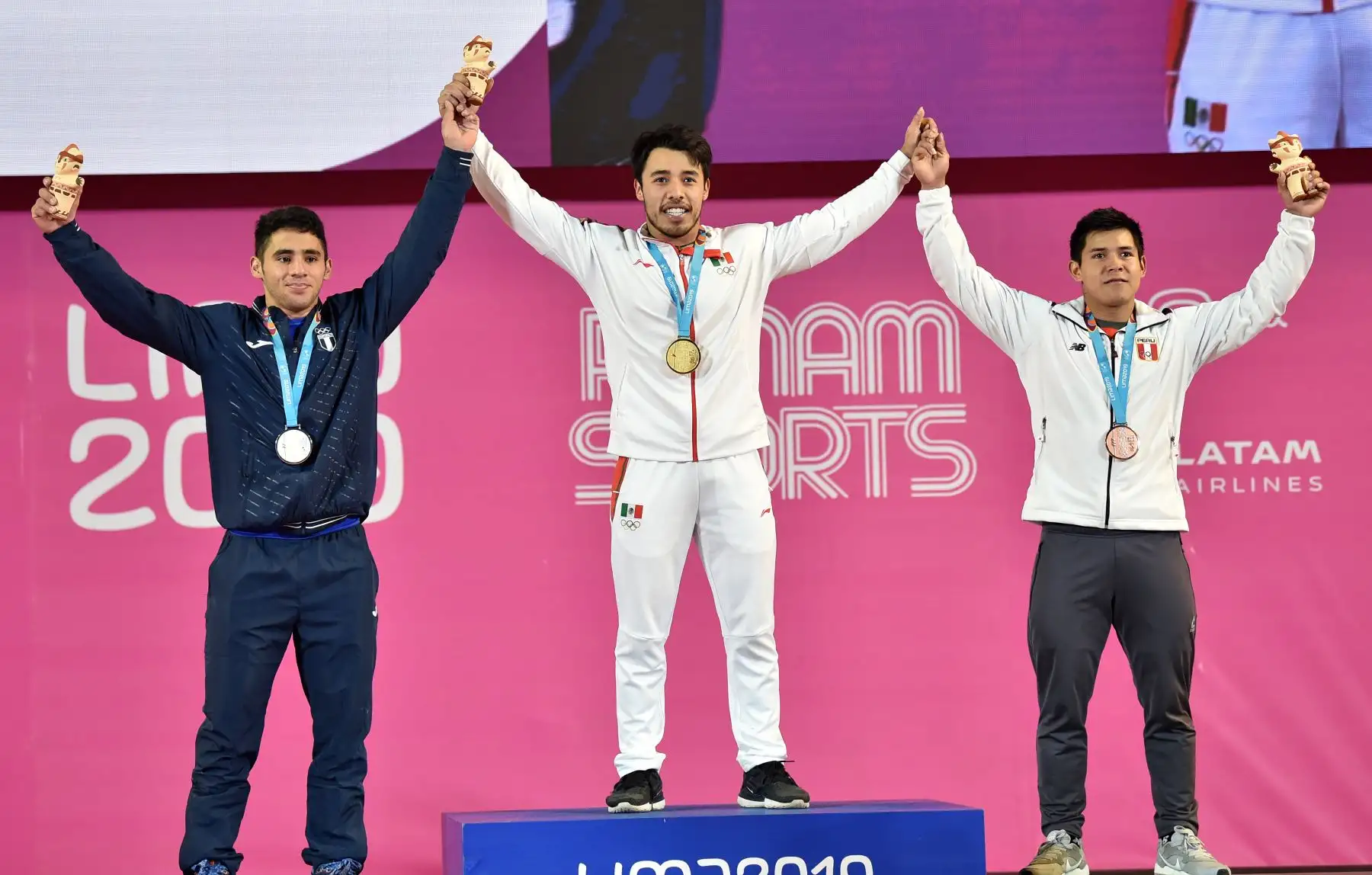 El mexicano Jonathan Muñoz (C), el guatemalteco Edgar Pineda (L) y el peruano Luis David Bardalez posan en el podio de la categoría Masculina de 67 kg del Grupo A en el evento de levantamiento de pesas con sus medallas de oro, plata y bronce, respectivamente, durante el torneo de Lima 2019.
Foto: AFP