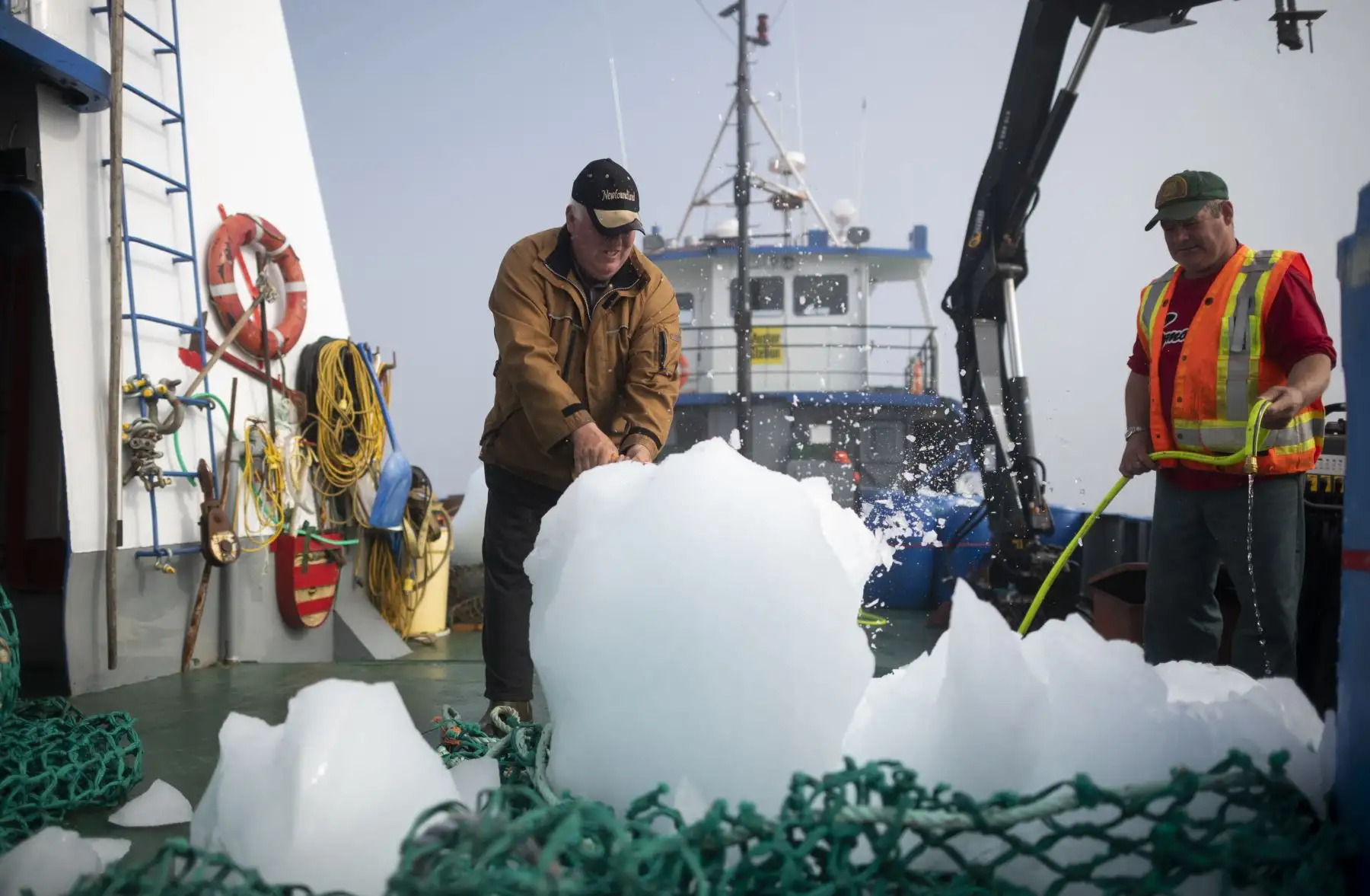 El Capitán Edward Kean  aplasta trozos de un iceberg, mientras que Phil Kennedy limpia el agua salada, mientras navegan en la Bahía de Bonavista en Terranova, Canadá.  Kean, un cazador de iceberg durante 20 años, ha estado navegando por el Atlántico Norte a bordo de su barco de pesca para recuperar trozos de hielo para derretir y vender el agua a los comerciantes locales. AFP