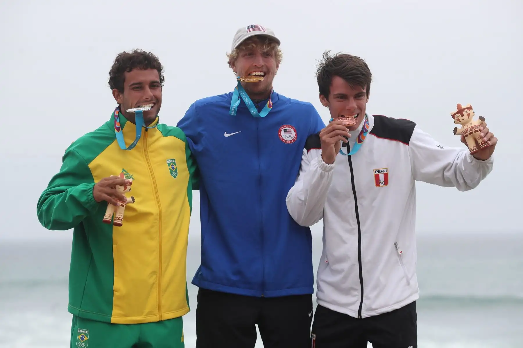 Connor Baxter (c) de Estados Unidos, medalla de oro, posa junto a Vinnicius Martins de Brasil, plata, y Itzel Delgado de Perú, bronce,  en la premiación de surf carrera SUP en los Juegos Panamerican Lima 2019.
Foto: AFP