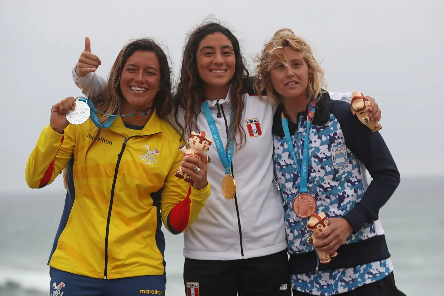 Daniella Rosas (c) de Perú, medalla de oro, posa junto a Dominic Barona (i) de Ecuador, plata, y Ornella Pellizzari de Argentina, bronce en la premiación de surf open femenino en los Juegos Panamwricanos Lima 2019.
Foto: EFE