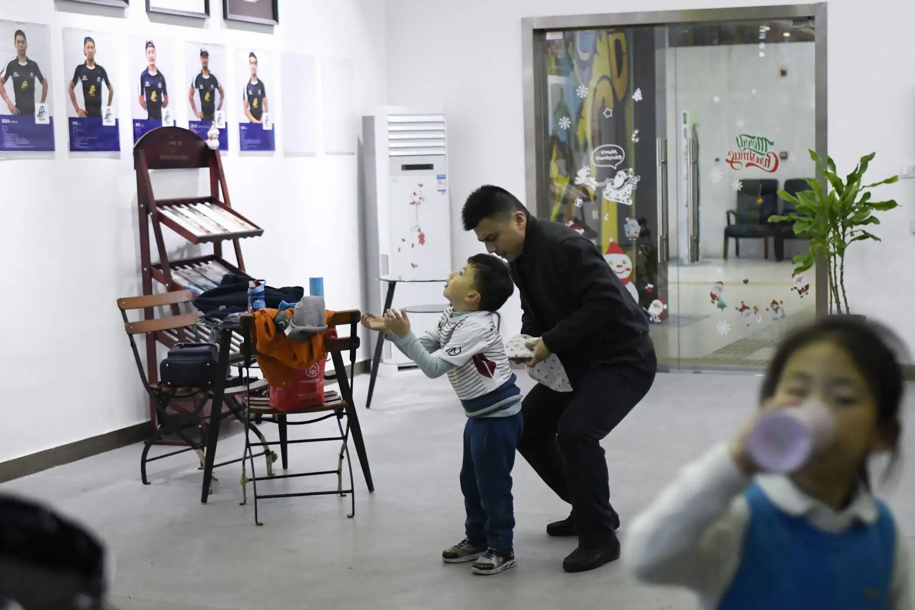 Niño  mirando retratos de jugadores de rugby en la pared mientras un hombre lo ayuda a cambiarse de ropa en un club juvenil de rugby en el municipio de Chongqing, suroeste de China.  AFP