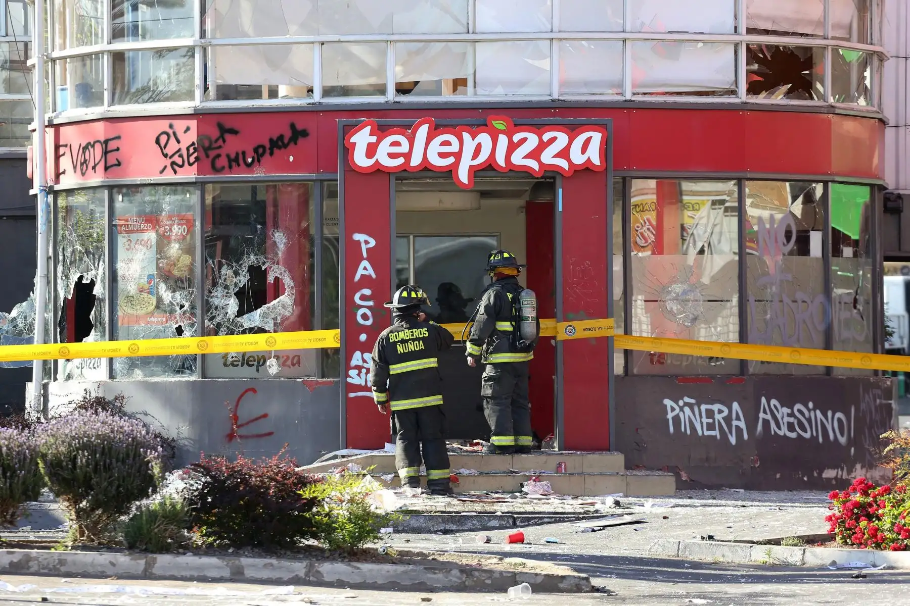 Personal policial y bomberos inspeccionan un local de pizzas después de ser saqueado e incendiado por manifestantes, en medio de la coyuntura de protestas en Santiago. Foto: EFE