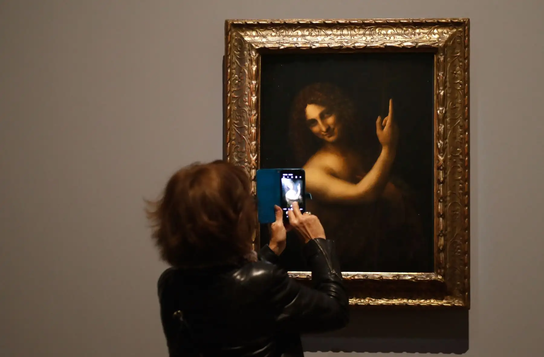 Una mujer toma una fotografía de una pintura al óleo sobre madera de nogal de "Saint Jean-Baptiste" de Leonardo da Vinci. Foto: AFP