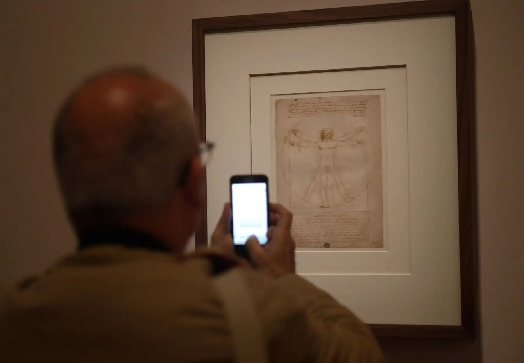 Un hombre toma una foto con un teléfono móvil en el "Hombre de Vitruvio", el famoso dibujo anotado, realizado alrededor de 1490 con pluma, tinta y lavado sobre papel, por Leonardo da Vinci. Foto: AFP