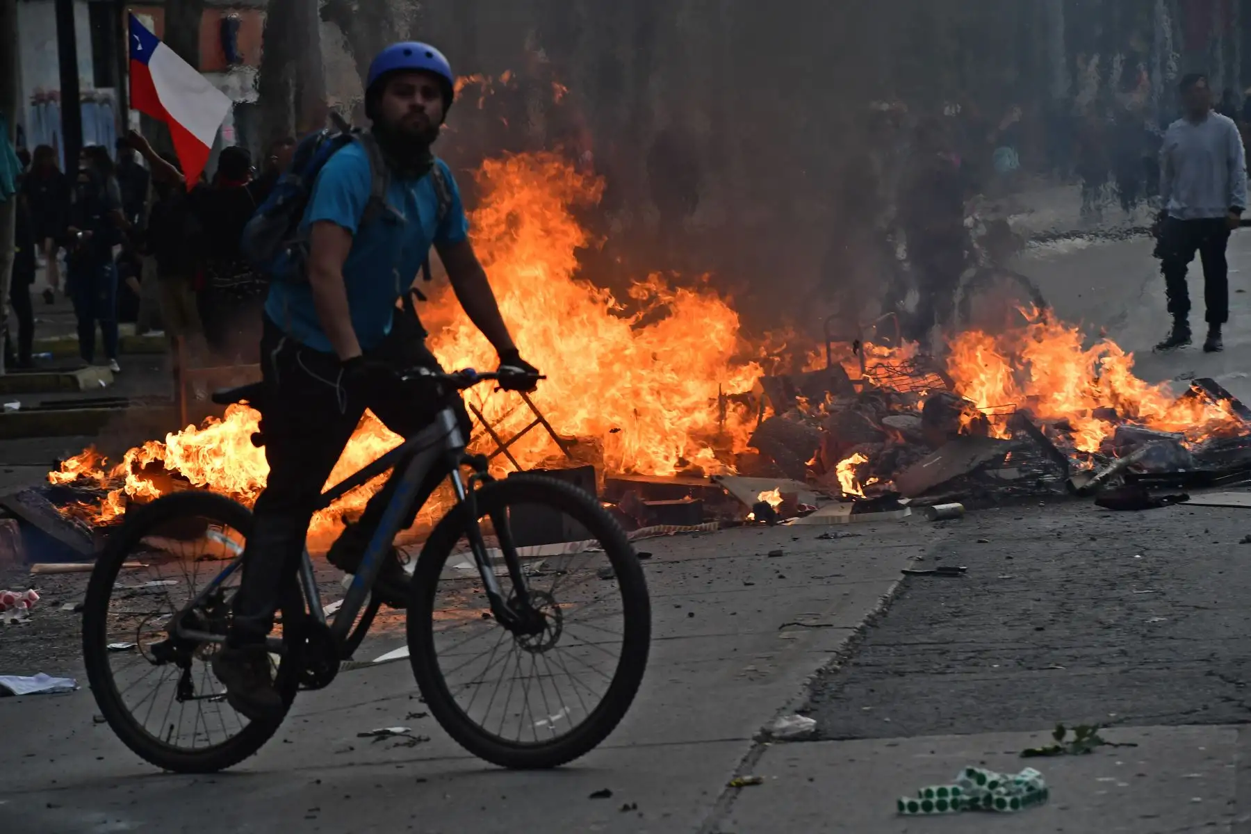 Un hombre monta una bicicleta frente a una hoguera en una barricada durante las protestas contra las políticas económicas del gobierno en los alrededores del palacio presidencial de La Moneda en Santiago.Foto:AFP