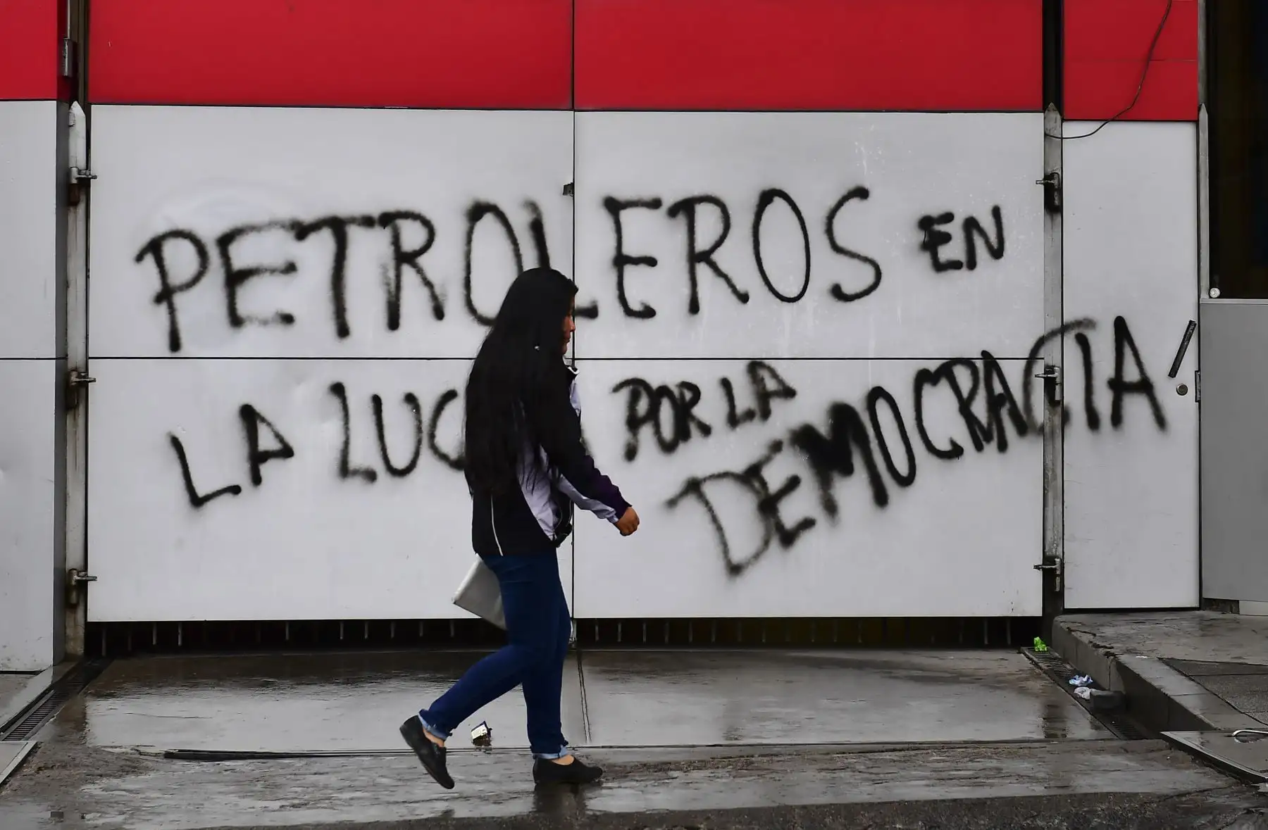 Una mujer camina junto a una pared con un graffiti que dice "Productores de petróleo en la lucha por la democracia" en La Paz. Foto: AFP