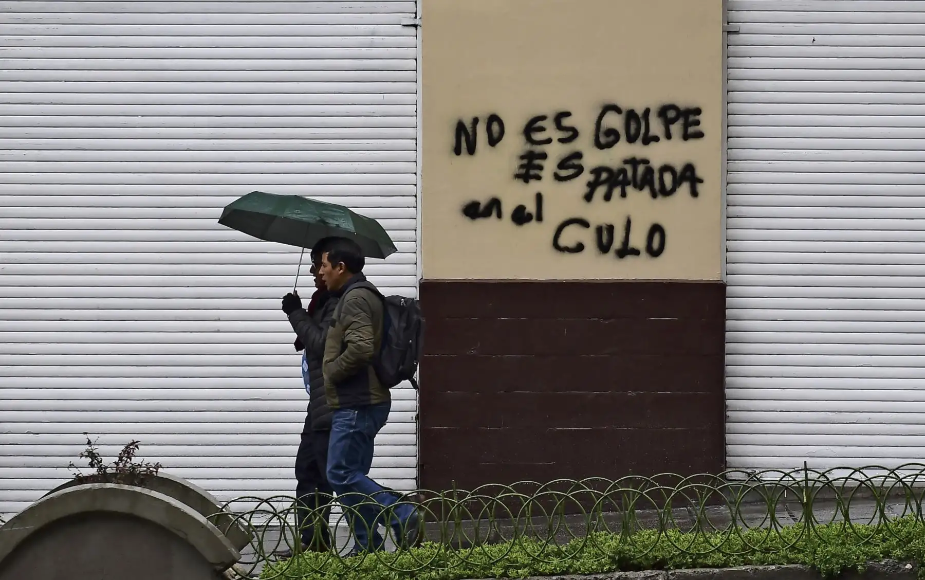 Dos hombres pasan junto a una pared con un graffiti que dice "No es un golpe de estado, es una patada en el culo" en La Paz. Foto: AFP