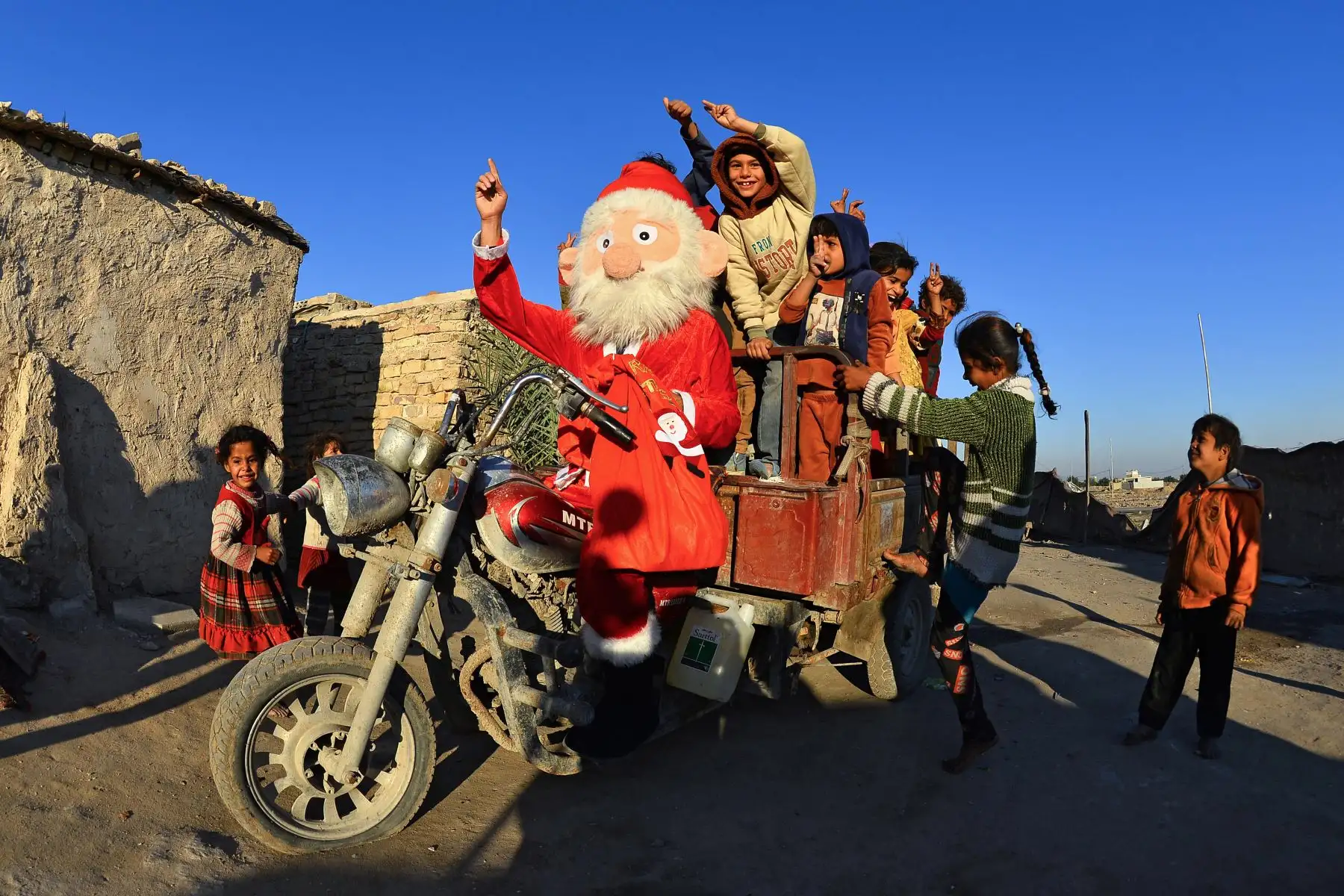 Niños iraquíes se suben a una motocicleta de tres ruedas conducida por un hombre vestido como Santa Claus distribuyendo regalos en Najaf. Foto: AFP