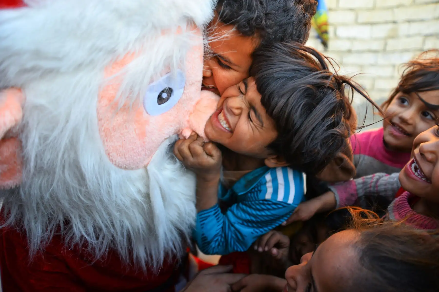 Niños iraquíes abrazan a un hombre disfrazado de Papá Noel mientras distribuye regalos en Najaf. Foto: AFP