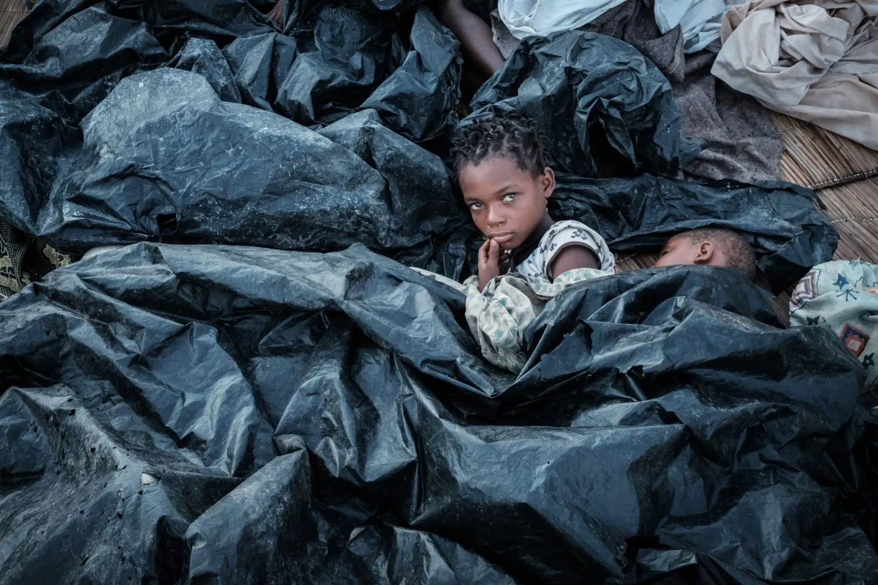 Enia Joaquín Luis, de 11 años, se despierta junto a su hermana Luisa, de 6 años, debajo de sábanas de plástico para protegerse de la lluvia mientras se refugian en las gradas de Ring Ground en Buzi, Mozambique. Foto: AFP