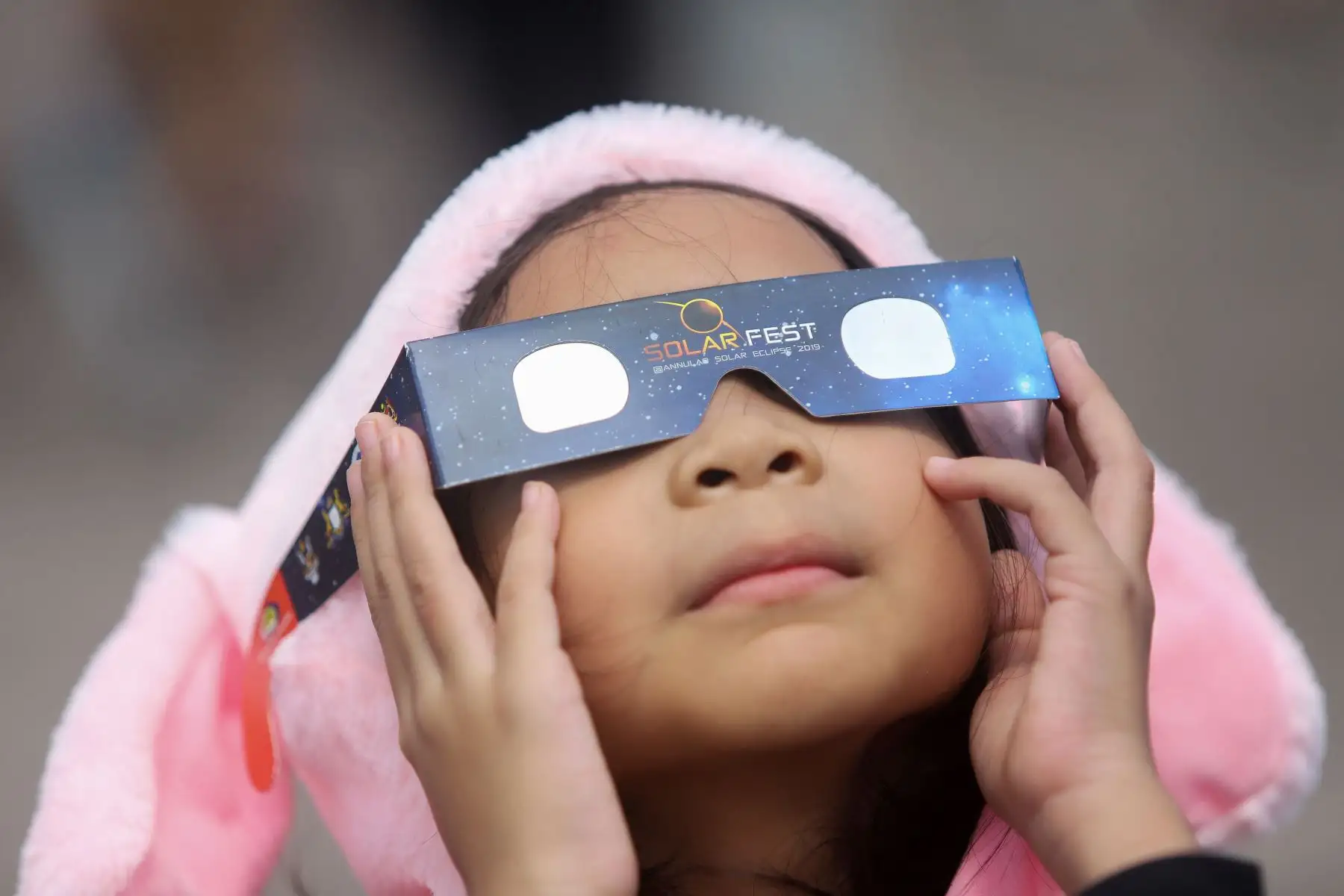 Una niña usa lentes de filtro solar para mirar la luna mientras se mueve frente al sol en un eclipse solar de "anillo de fuego" en Tanjung Piai, Malasia. Foto: AFP