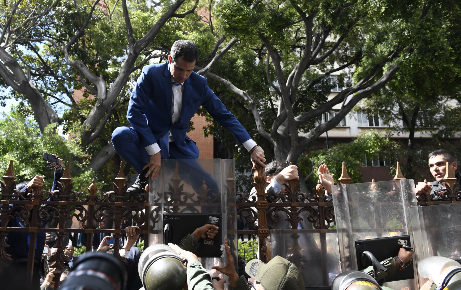 El líder de la oposición venezolana y autoproclamado presidente en funciones, Juan Guaido, recibe ayuda para subir una barandilla en un intento de llegar al edificio de la Asamblea Nacional en Caracas.
Foto: AFP