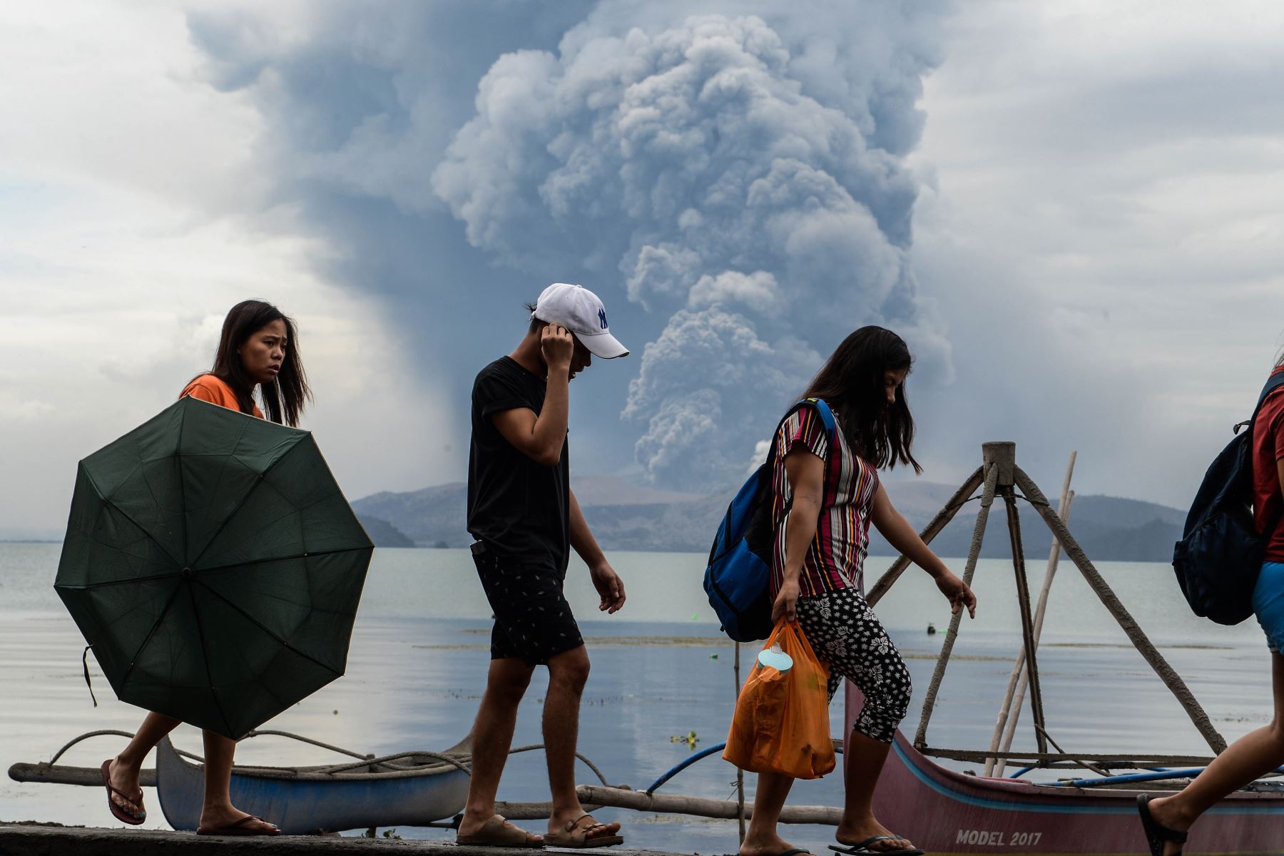Residentes pasan junto a barcos de madera cuando el volcán Taal hace erupción al sur de Manila. Foto: AFP
