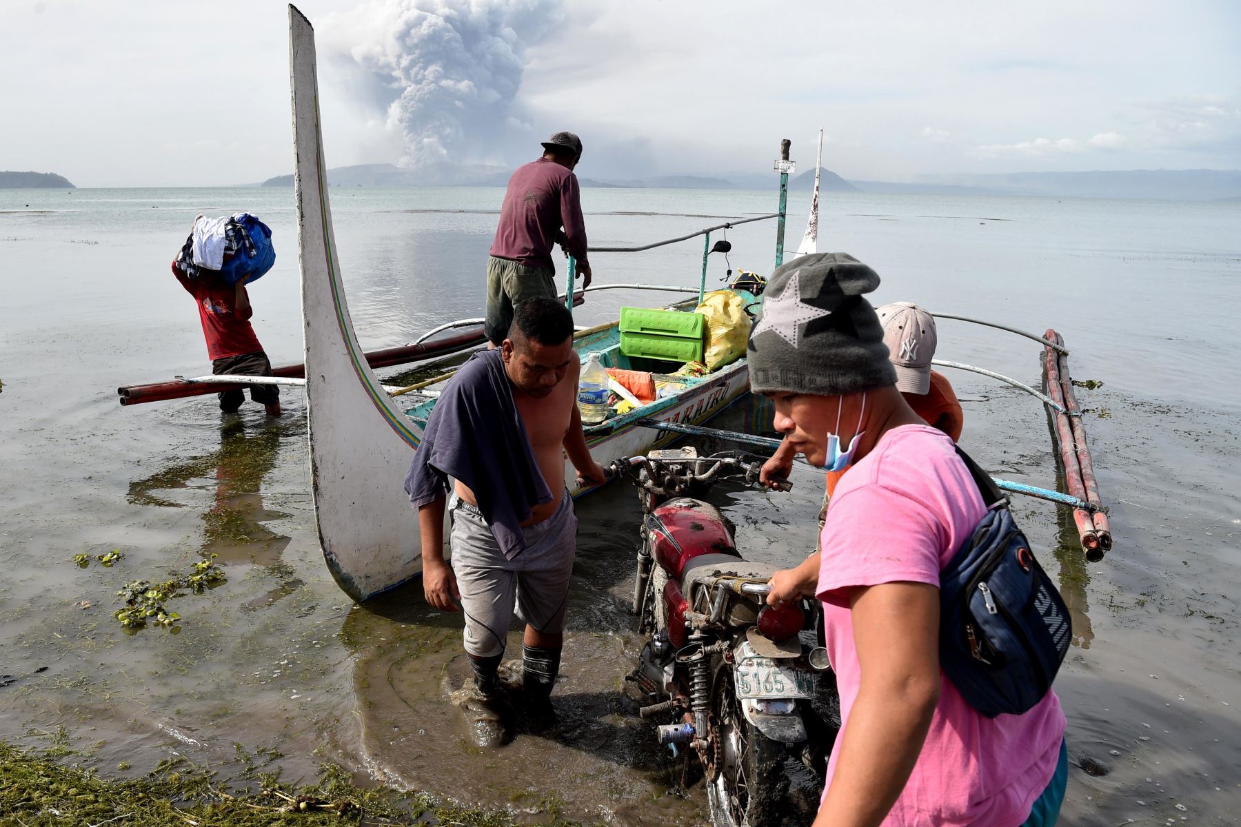 Residentes evacuados que viven al pie del volcán Taal descargan sus pertenencias de una canoa estabilizadora mientras el volcán arroja cenizas. Foto: AFP