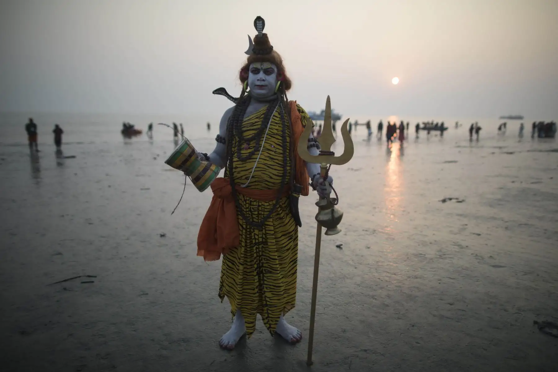 Un devoto hindú vestido como Lord Shiva se para en la playa mientras otros se bañan en la bahía de Bengala durante el Gangasagar Mela, en la isla Sagar, a unos 150 kilómetros al sur de Calcuta. Foto: AFP