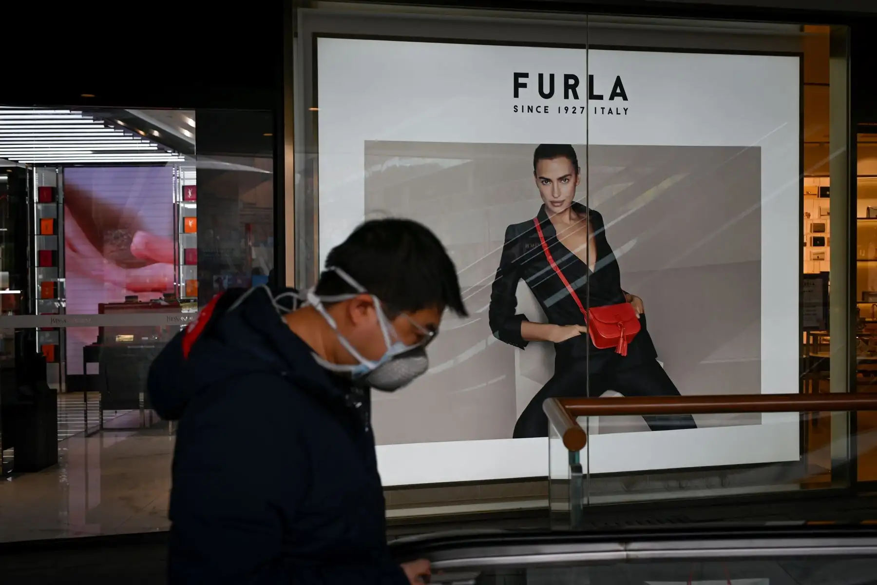 Un hombre con una máscara facial camina por un centro comercial en Beijing. Foto: AFP