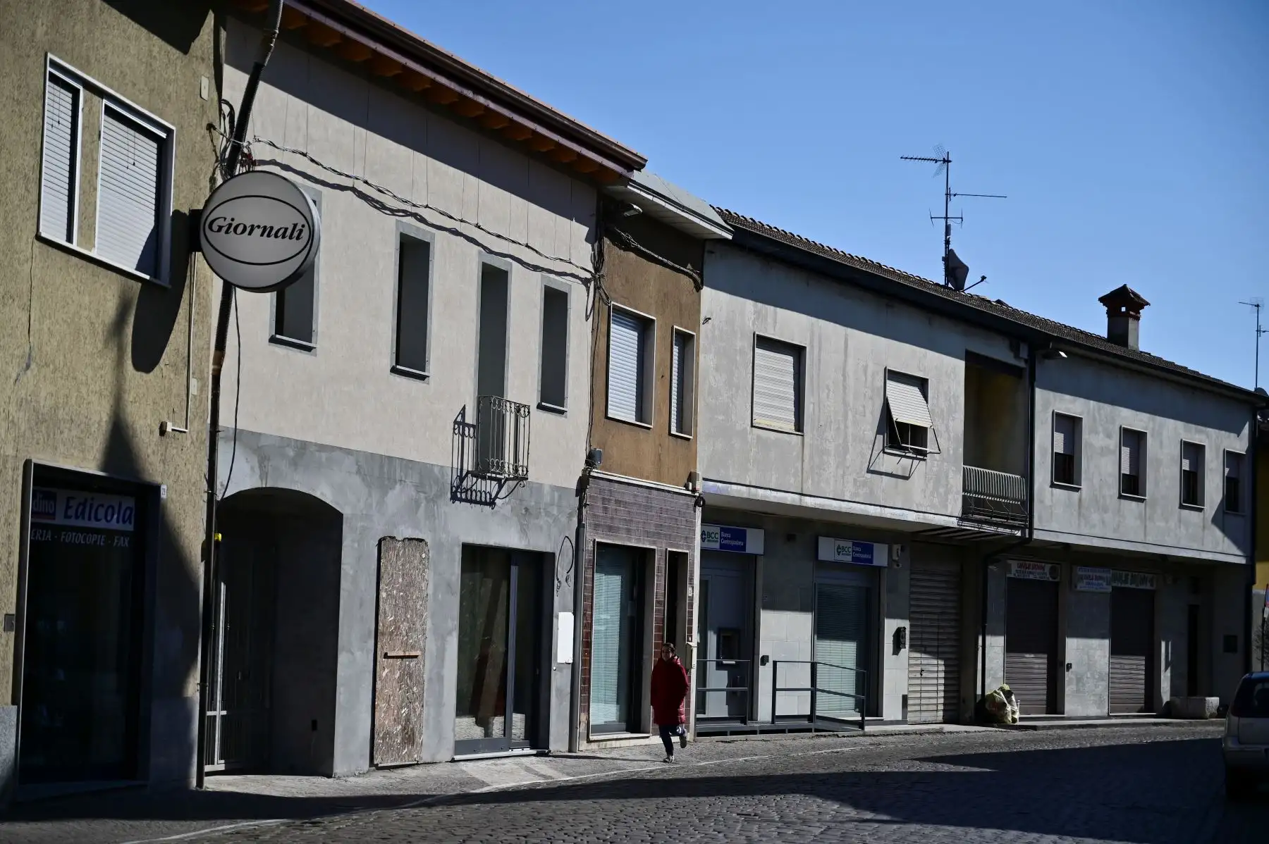 Una mujer pasa por las tiendas cerradas a lo largo de la calle principal de Secugnano, el pueblo más cercano a Zorlesco, al sureste de Milán,que se encuentra en la zona roja del COVID-19, el nuevo brote de coronavirus en el norte de Italia. AFP