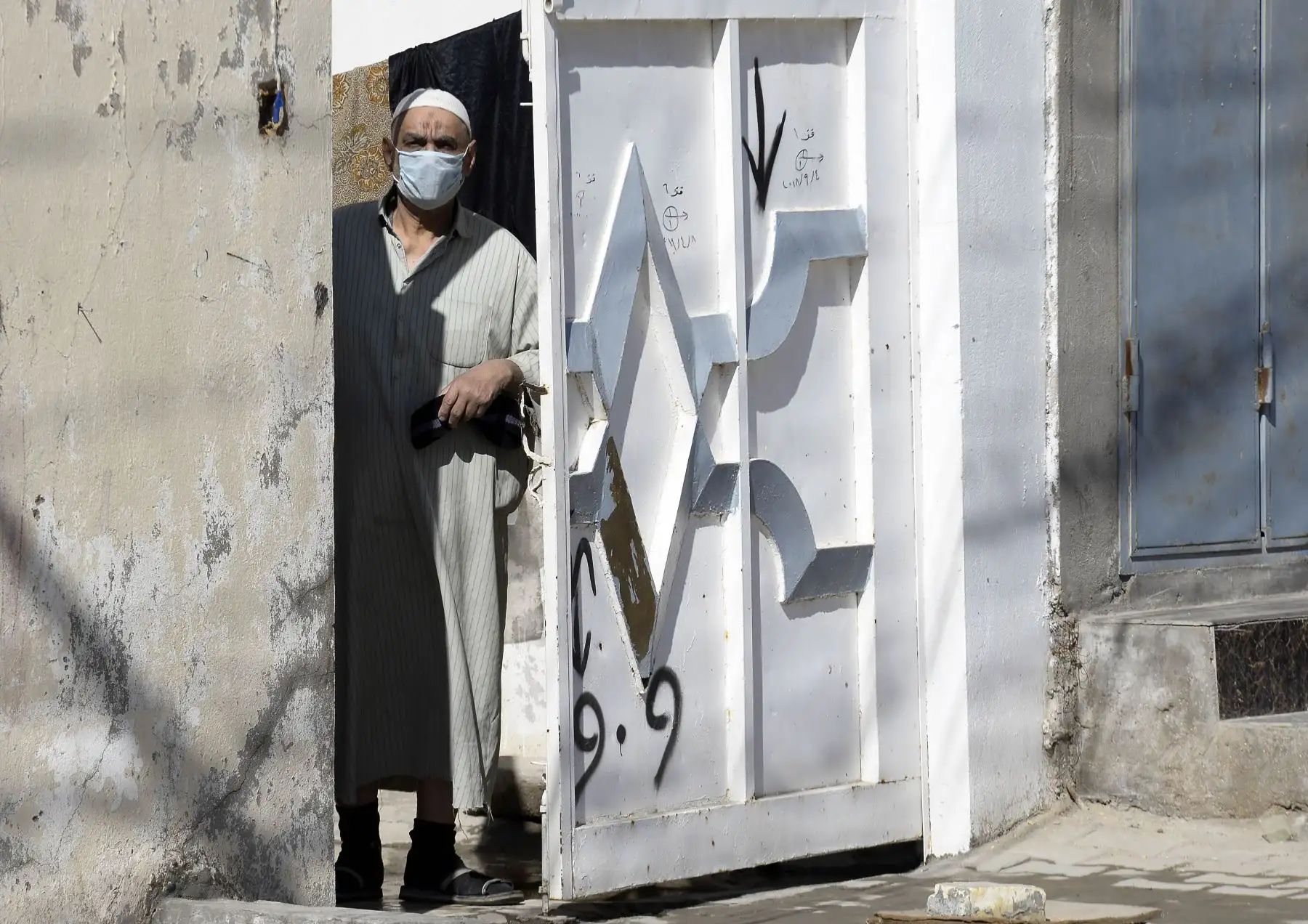Un hombre iraquí con una máscara protectora mira por una puerta de entrada mientras los miembros de la defensa civil desinfectan un vecindario donde se confirmó un caso reciente de infección por coronavirus en el santuario central de la ciudad de Najaf.
Foto: AFP