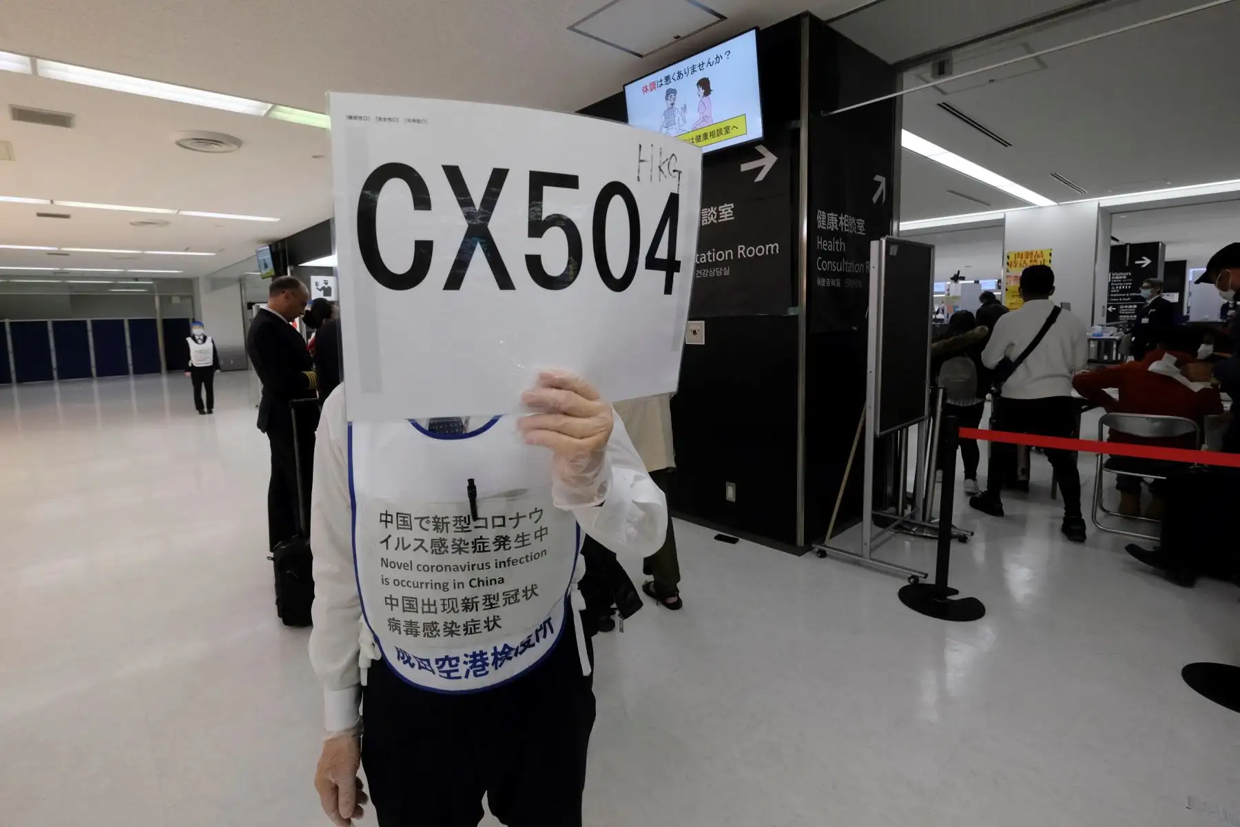 Un oficial que usa guantes protectores ayuda a los pasajeros que llegan desde Hong Kong, a una estación de cuarentena en el aeropuerto de Narita en Japón. Foto: AFP