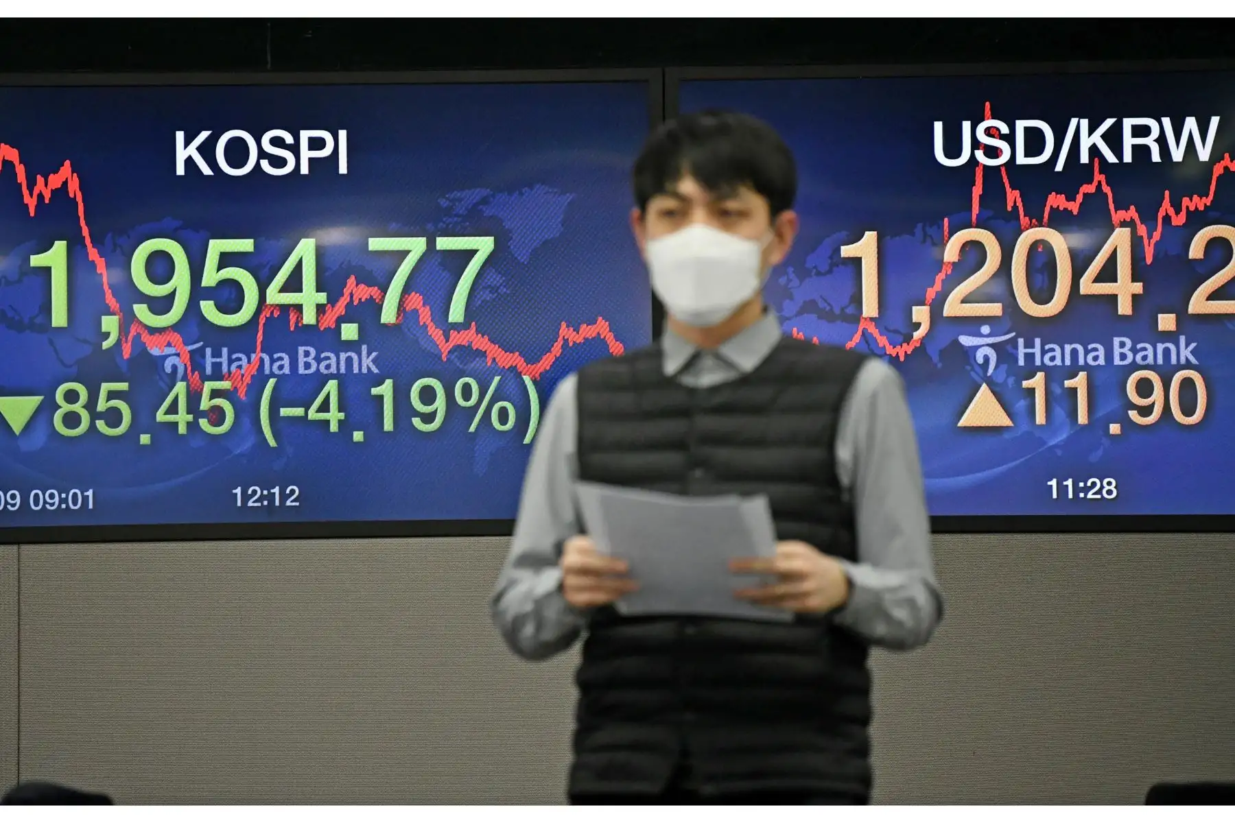 Un comerciante de divisas con una máscara facial pasa frente a las pantallas que muestran el índice bursátil de referencia de Corea del Sur. Foto: AFP