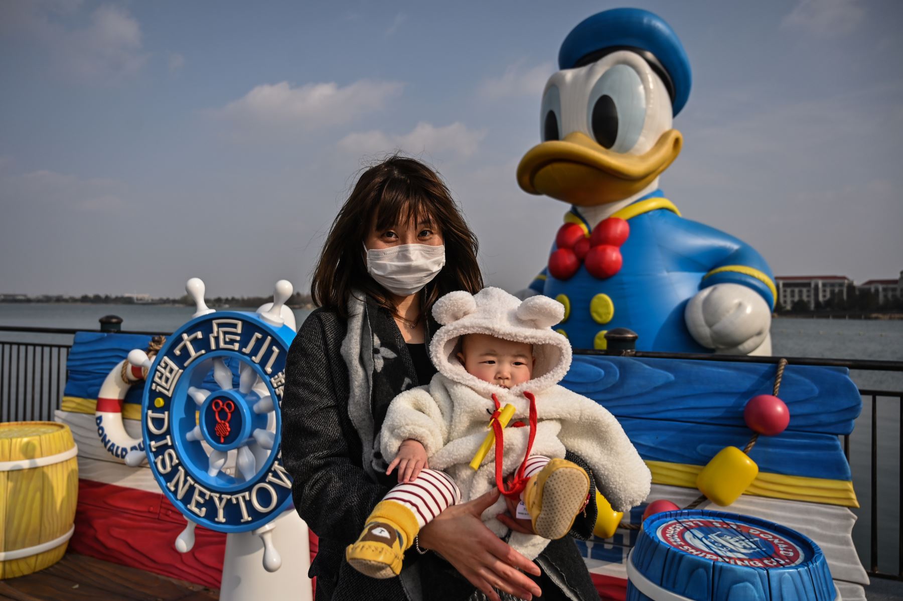Una mujer que usa una máscara facial como medida preventiva contra el coronavirus COVID-19 sostiene a un niño mientras visita Disneytown en Shanghai. Foto: AFP