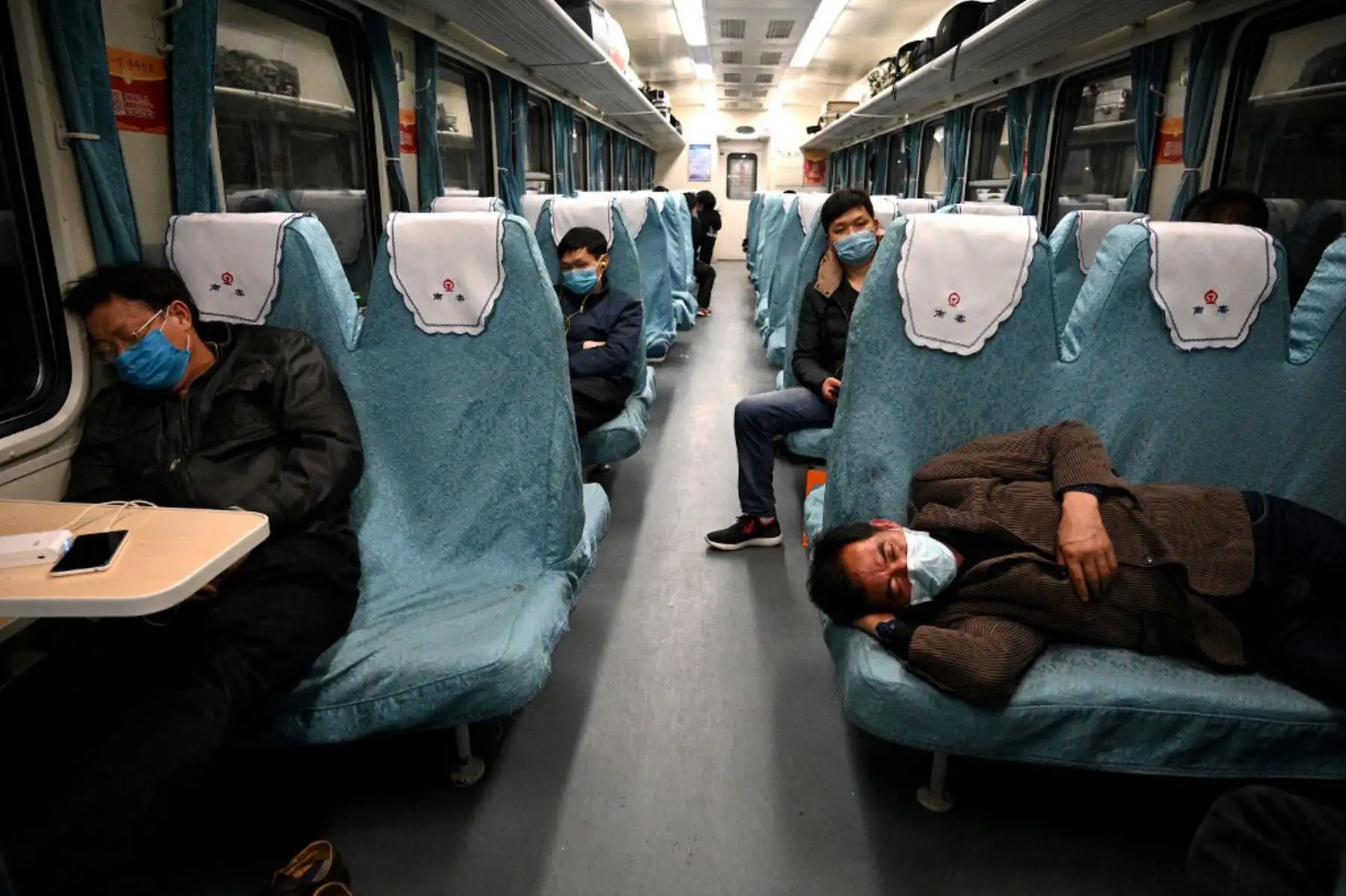 Pasajeros que llevan mascarillas duermen mientras el tren se detiene en la estación de ferrocarril de Dongzhi, en China. Foto. AFP