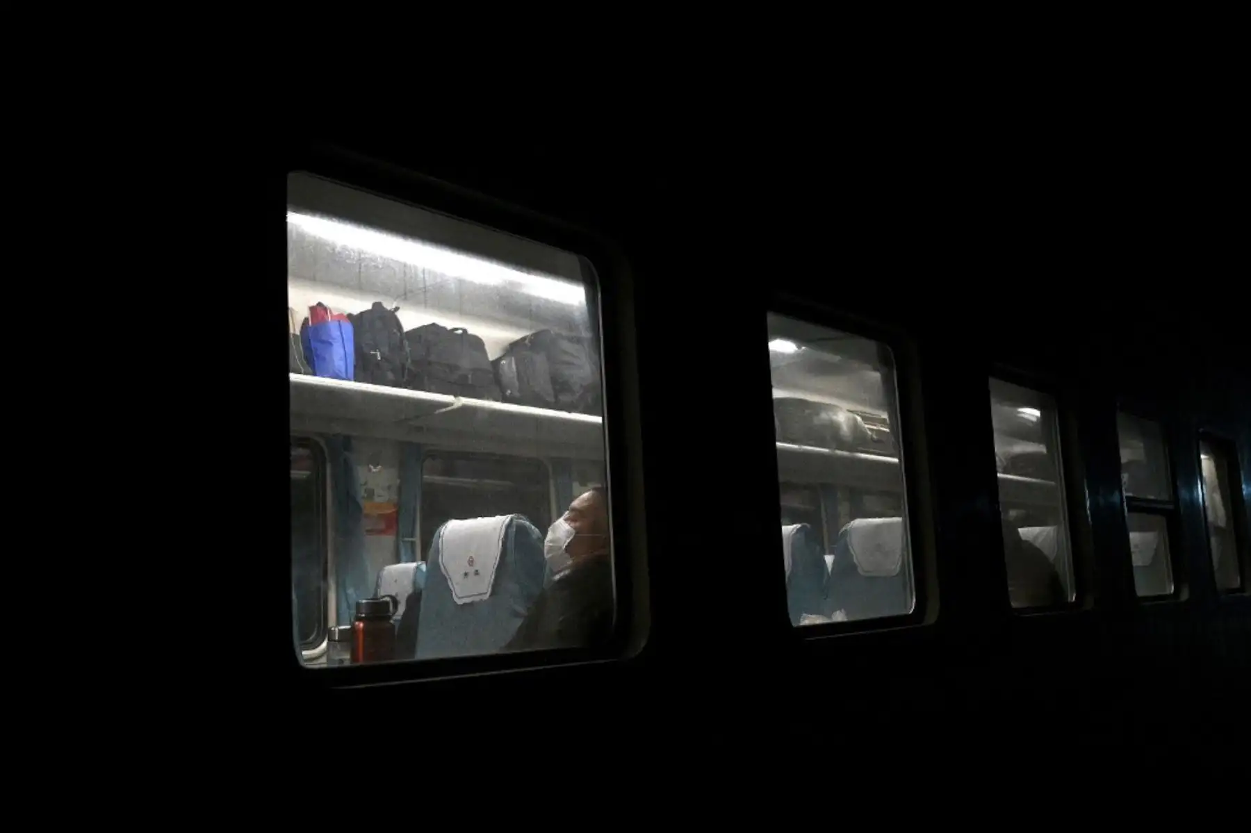 Un pasajero con una máscara facial duerme mientras el tren se detiene en la estación Dongzhi en China. Foto: AFP