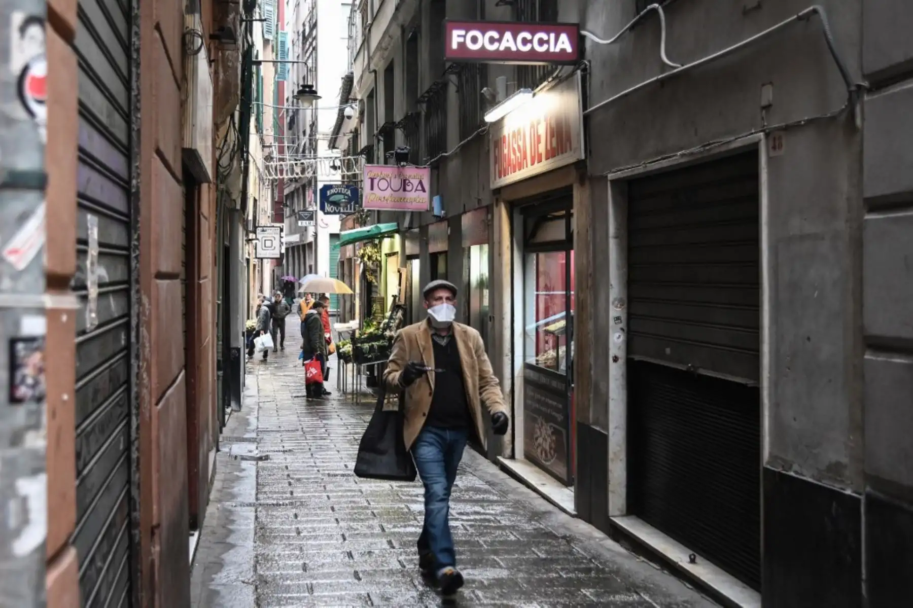 Un residente transita con protección con mientras realiza habituales compras  de alimentos típicos, en el laberinto de callejones de la histórica Génova. Foto: AFP