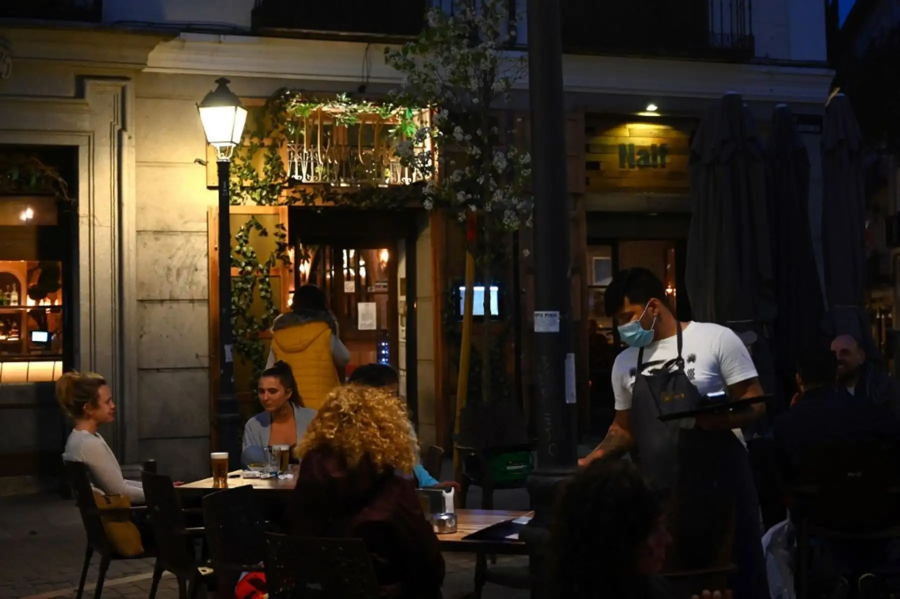 Un camarero usa una mascarilla protectora mientras las personas se sientan en una terraza en Madrid. Foto: AFP